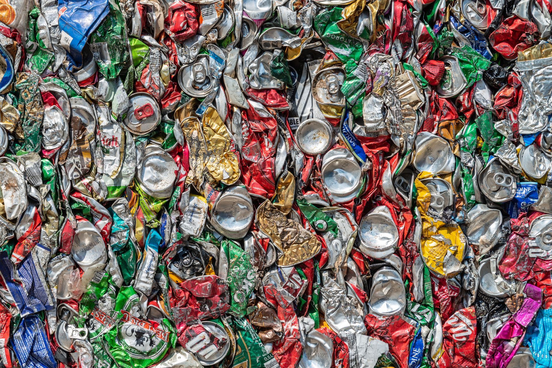 A dense, colorful pile of crushed aluminum cans in various shades of blue, red, green, silver, and gold.