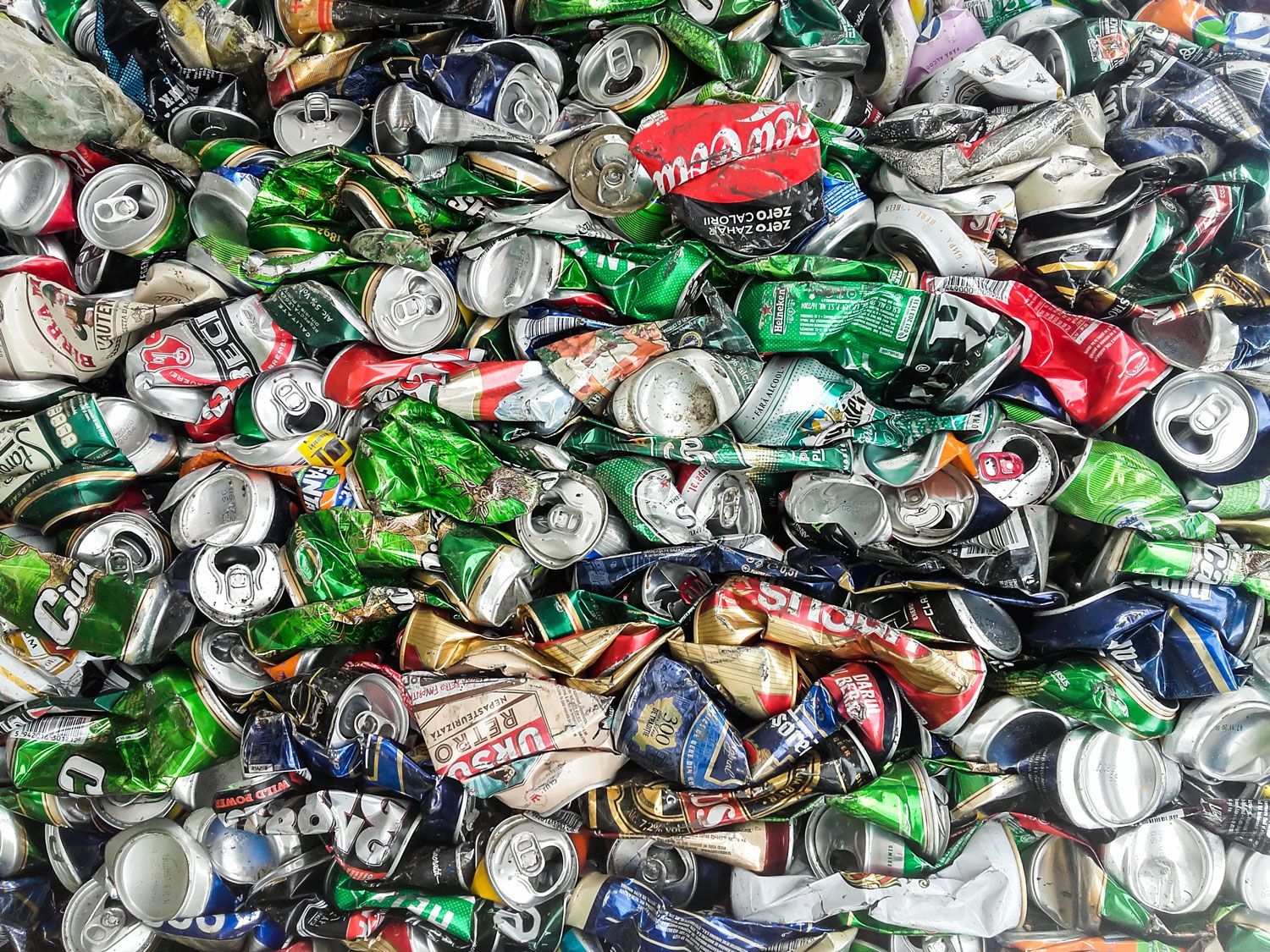 A large, chaotic pile of flattened, colorful aluminum beverage cans ready for recycling.