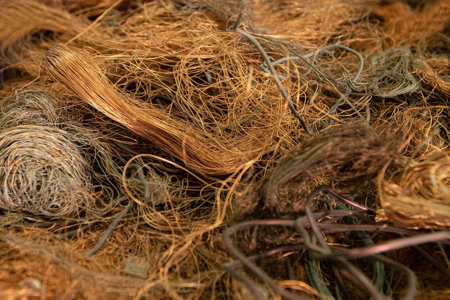 A close-up of tangled copper and other wires. A jumbled pile of textured, copper-colored wire strands and metallic fibers.