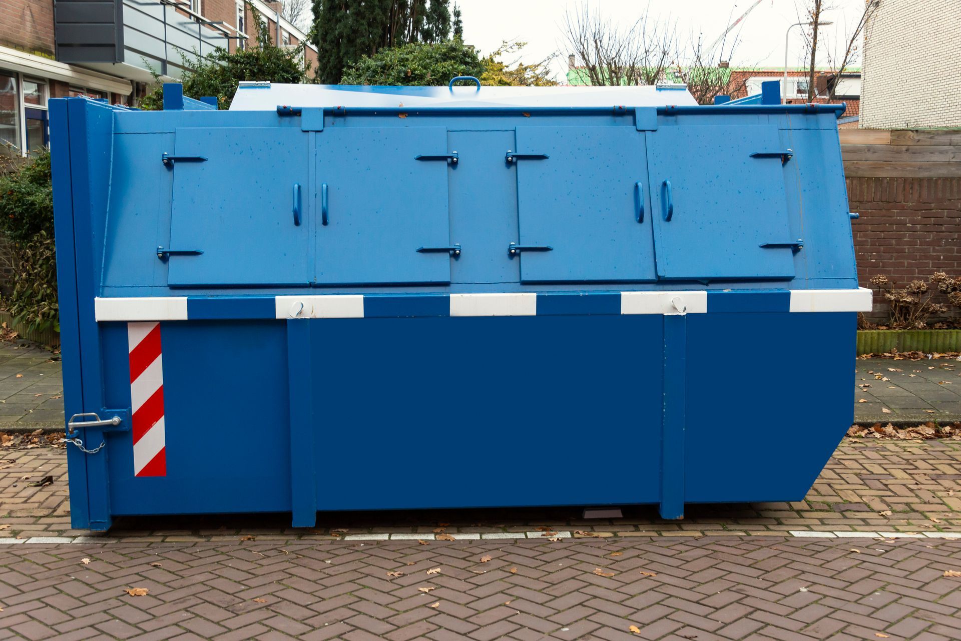 A large, bright blue metal dumpster with multiple hinged lids sits on a paved street.