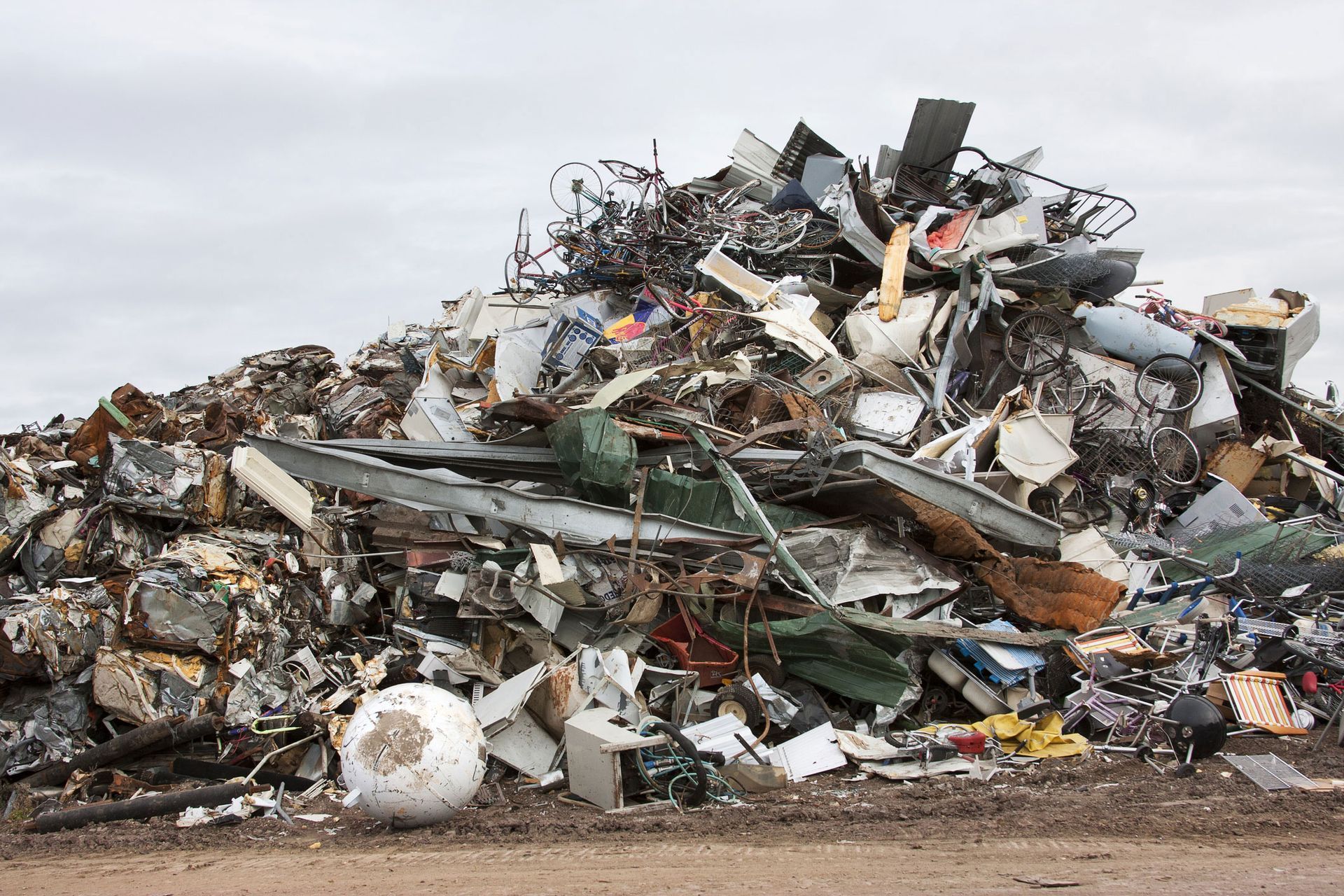 A large, chaotic pile of mixed metal scrap, appliances, and debris under a cloudy sky.
