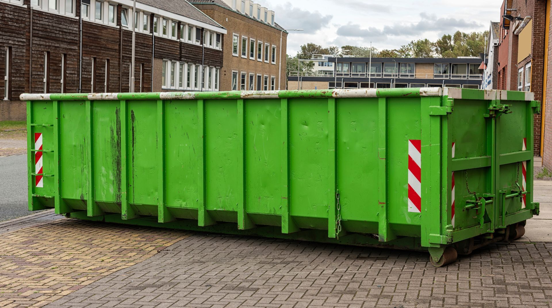 A large, empty bright green roll-off dumpster sitting on a paved surface in front of a building.