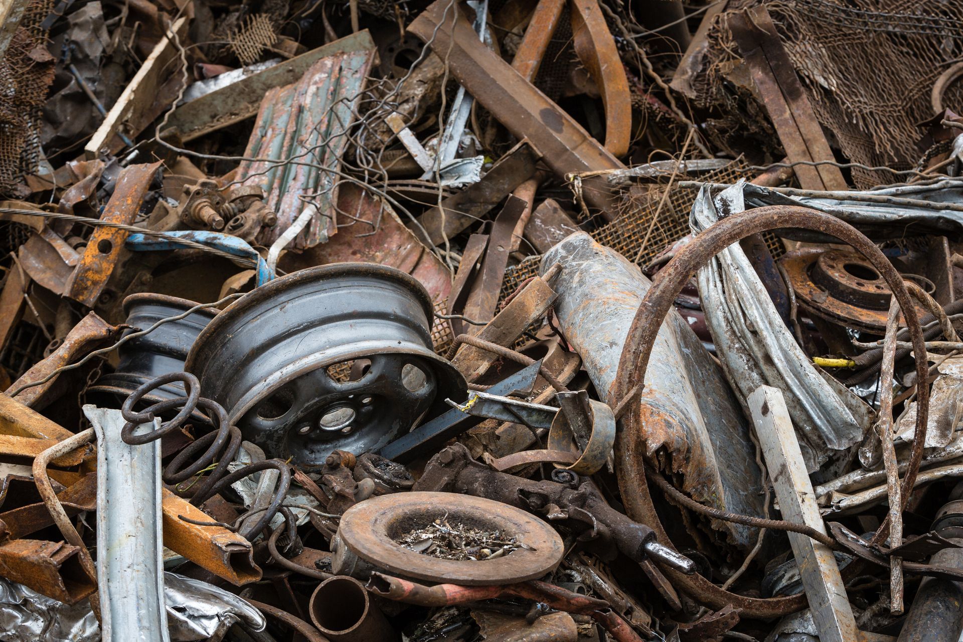 A jumbled pile of rusted metal scrap, including old car wheels, metal beams, and fragmented steel parts.