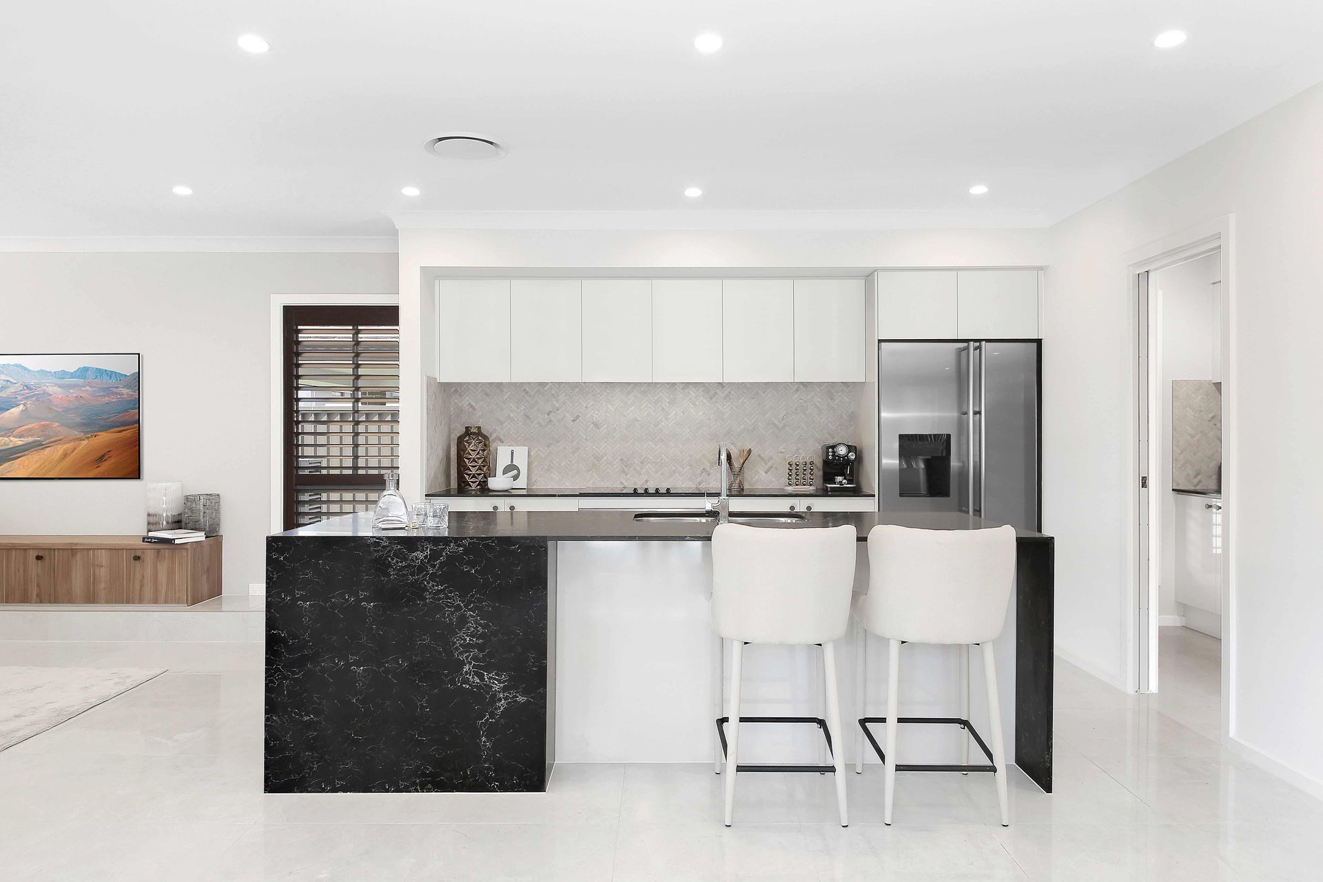 Riviera 28 home design of a kitchen with white cabinets, a black counter top, a refrigerator, and two bar stools.