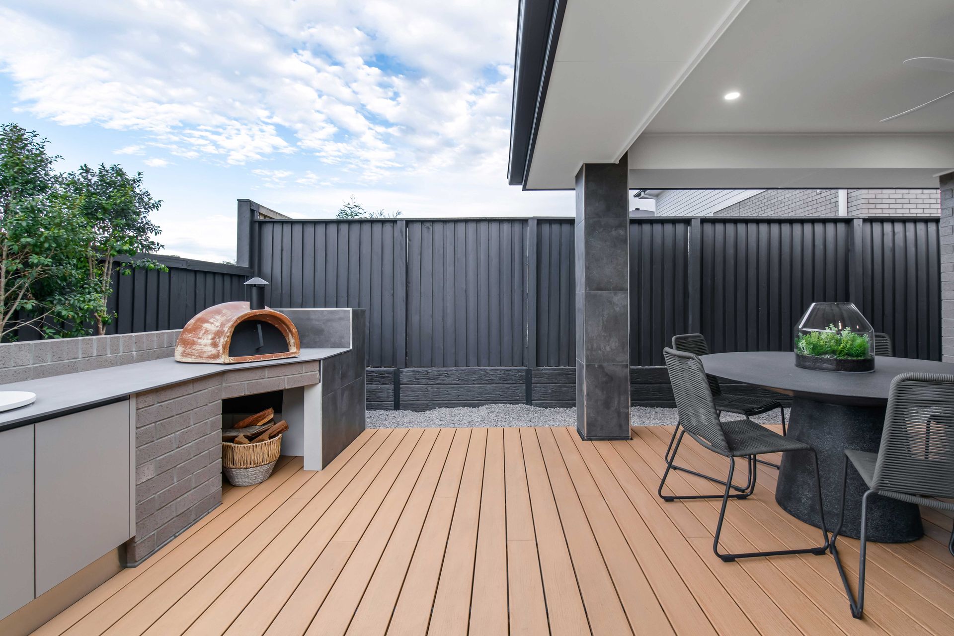 Refuge 27 home design - A wooden deck with a table and chairs and a pizza oven.