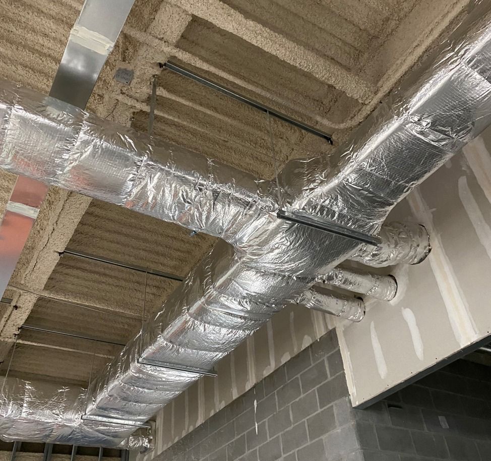 Industrial ceiling with silver insulated ductwork and exposed beams in a construction site