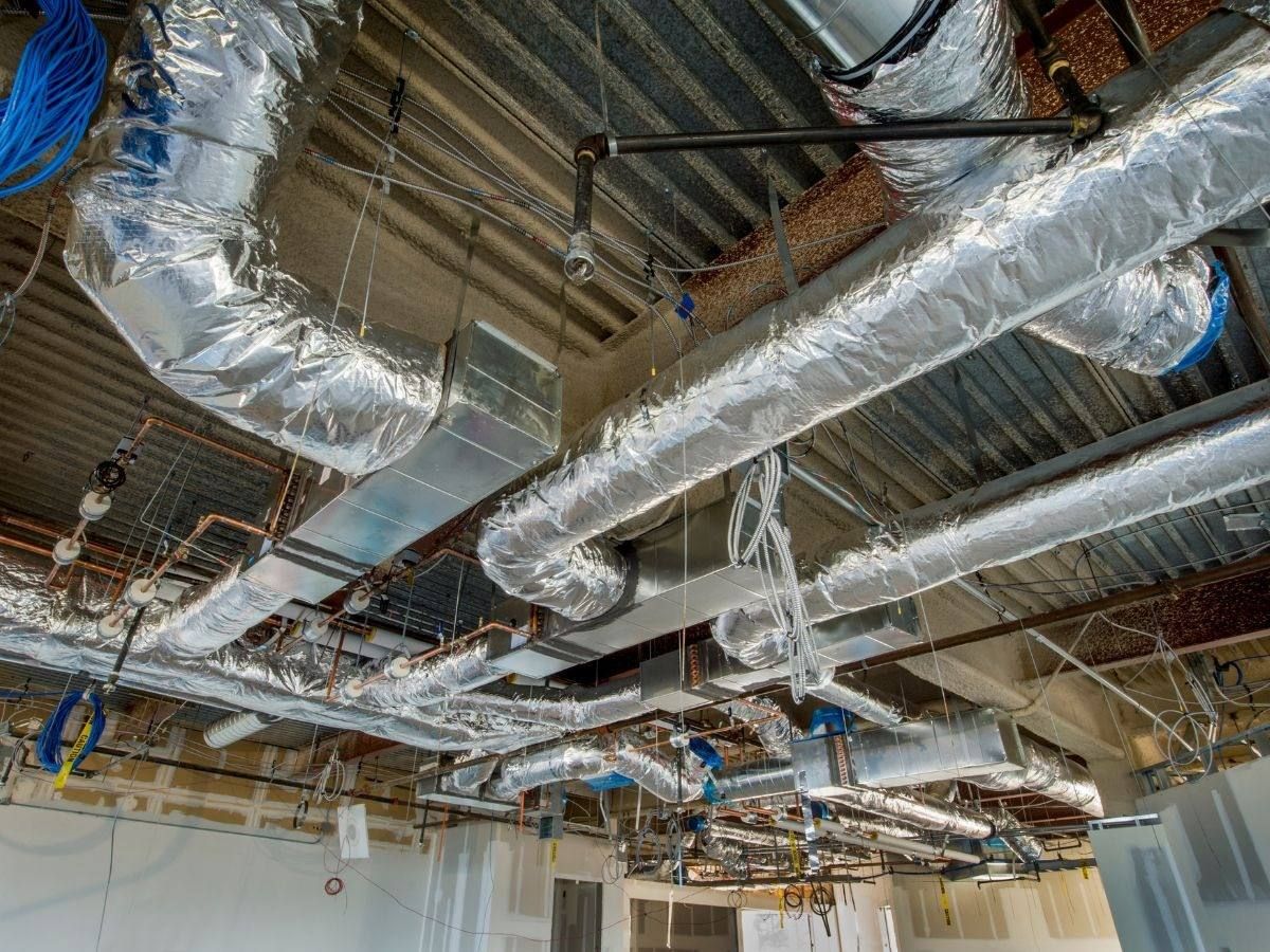 Exposed ceiling with silver HVAC ducts and pipes in an unfinished building interior