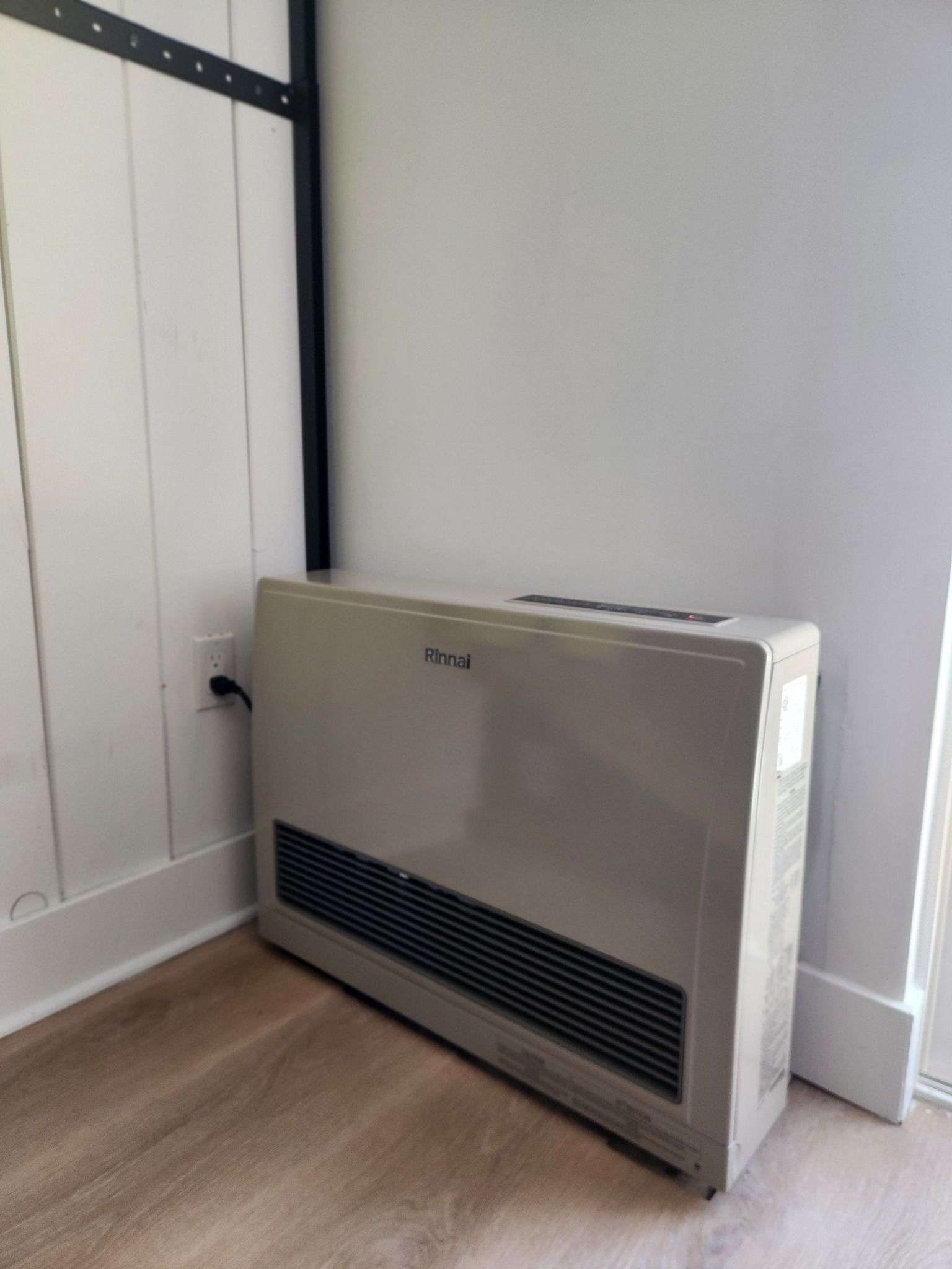 Wall-mounted heater in a corner beside white paneled doors and a light wood floor