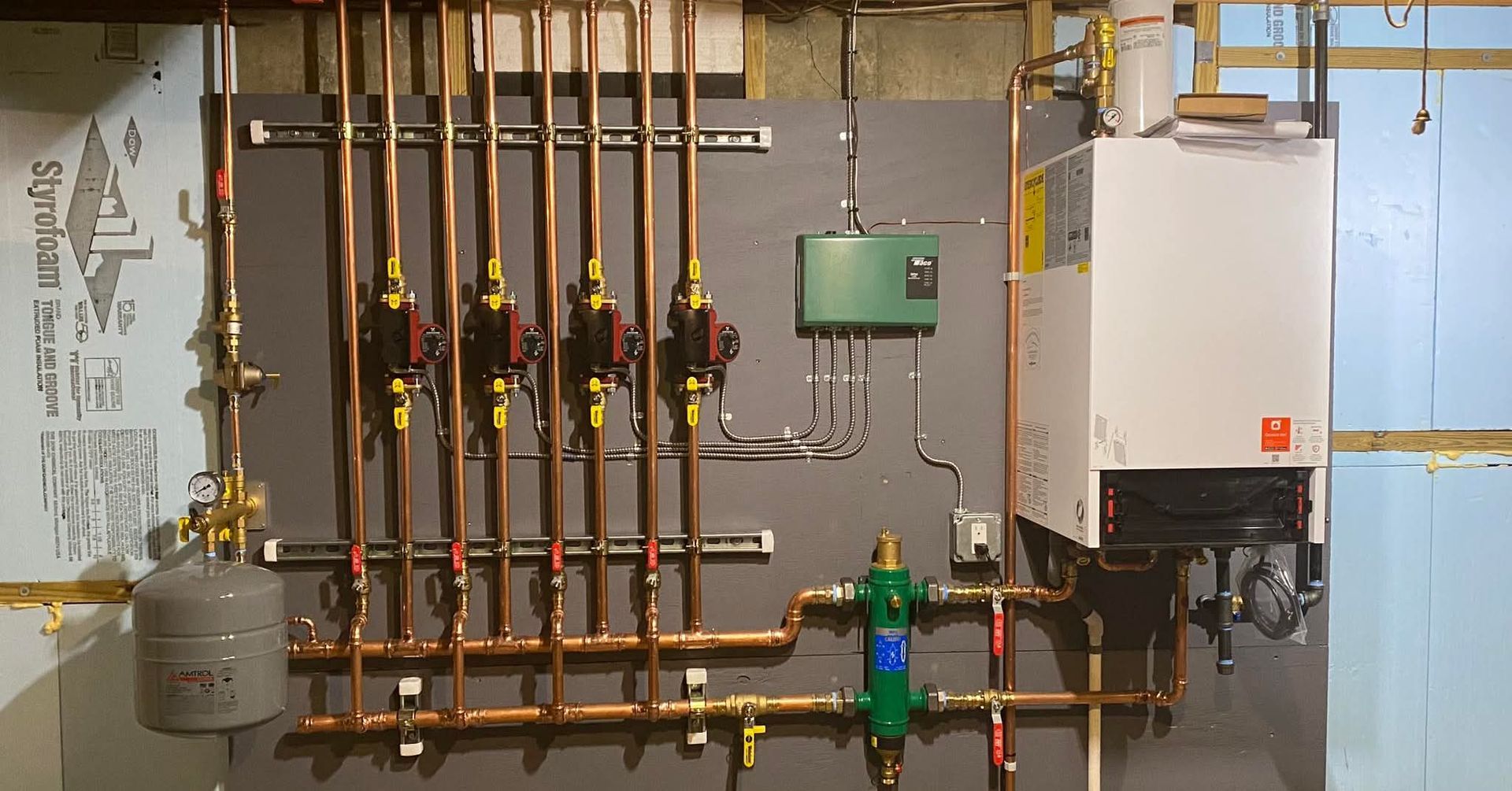 Boiler room with copper pipes, valves, tanks, and wall-mounted heating equipment.