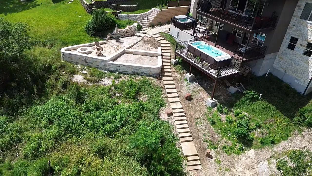 Aerial view of a house with a small pool, stone patio, and steps through lush green vegetation.