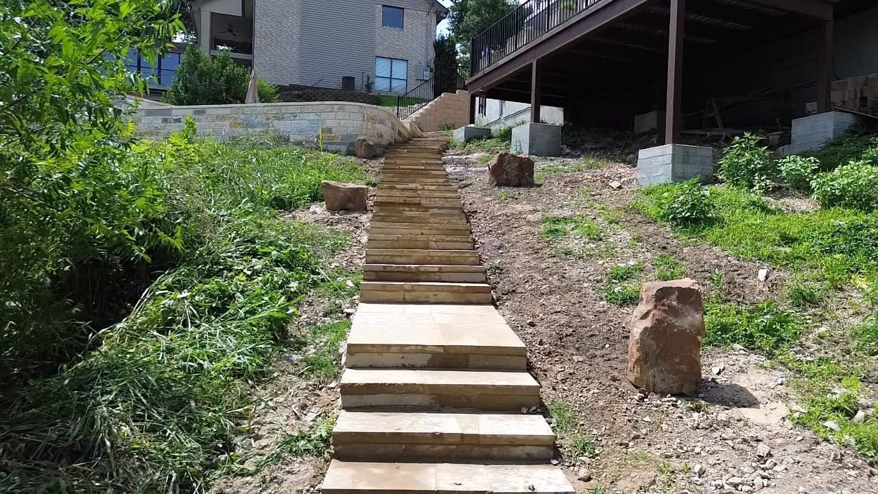 Steep outdoor stone stairway leading up a grassy hillside beside a building and wooden deck