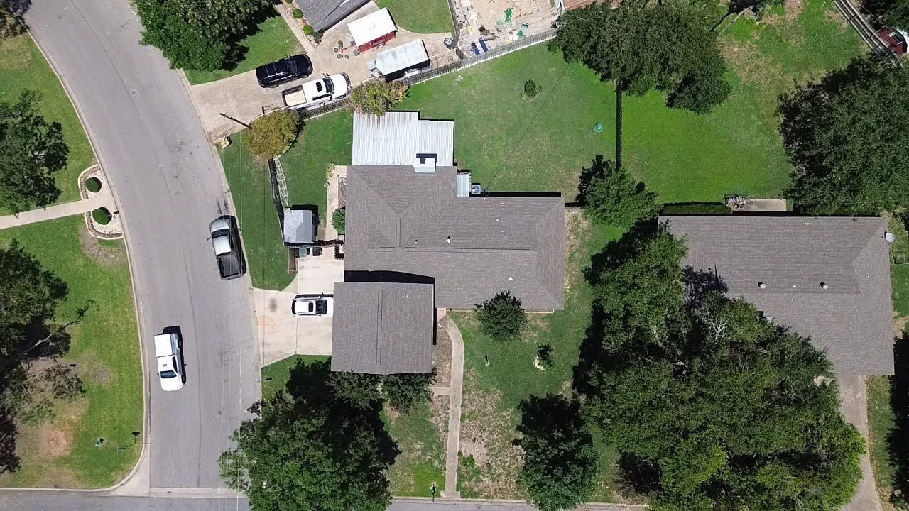 Aerial view of a suburban house with driveway, parked cars, and green lawns.