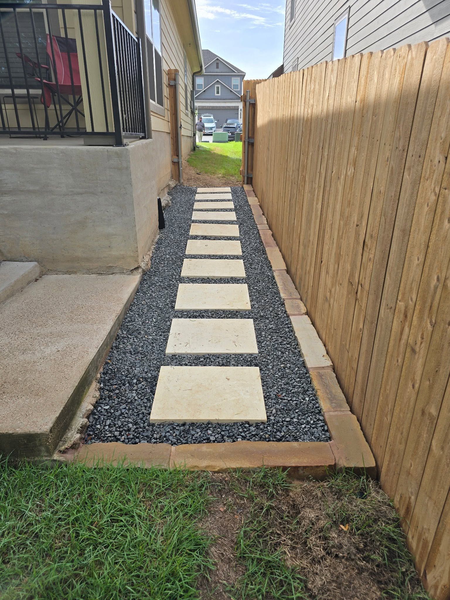 Narrow gravel walkway with stepping stones beside a house and wooden fence, leading to a backyard.