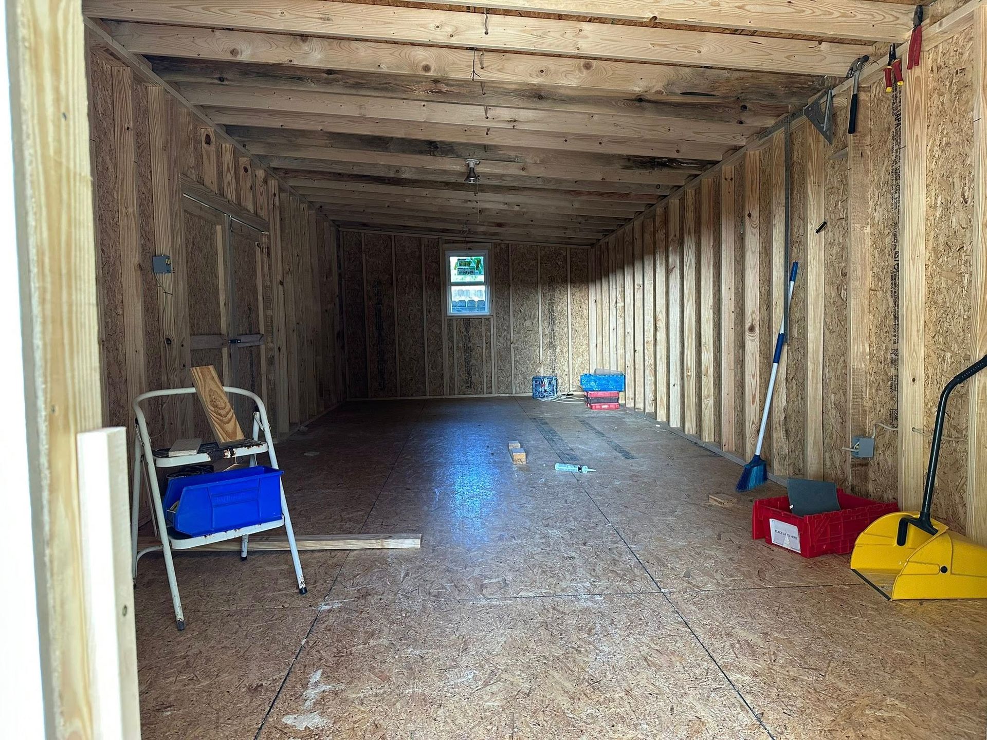 Empty unfinished wooden interior with insulation, a step ladder on the left, and tools stored along the floor.