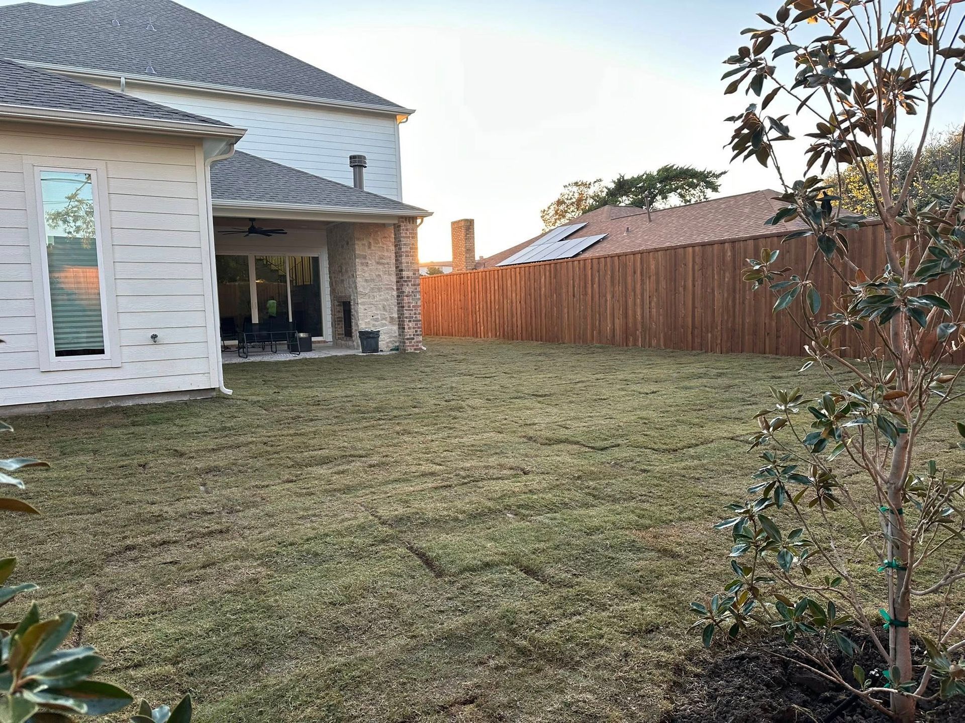 Backyard with freshly cut grass, a white house patio on the left, and a wooden fence along the right