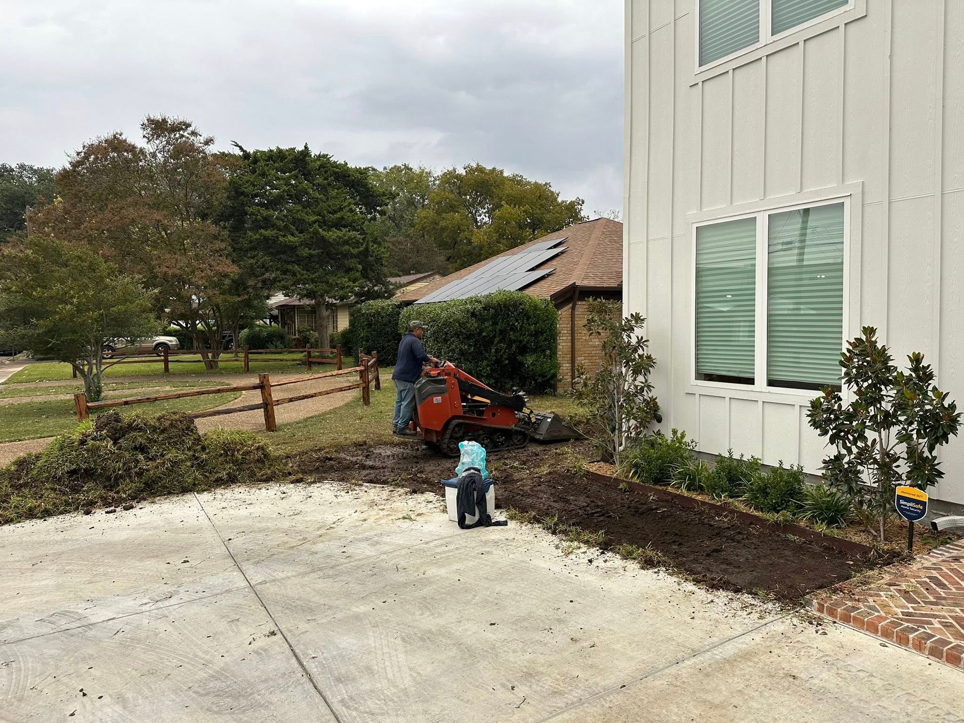 Person using a red lawn mower near a house beside a concrete driveway
