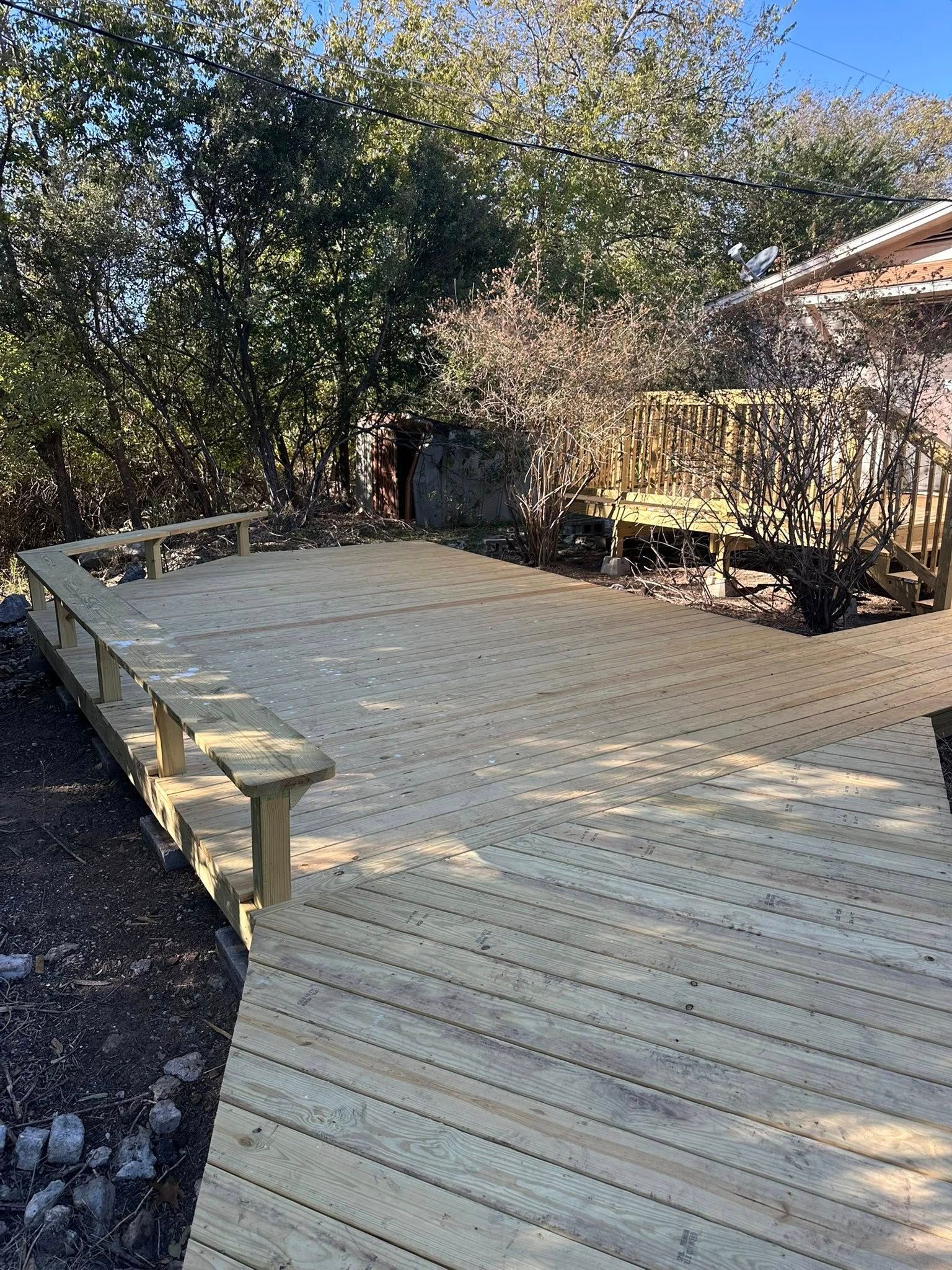 Wooden deck under construction beside a house, with railing and trees in the background