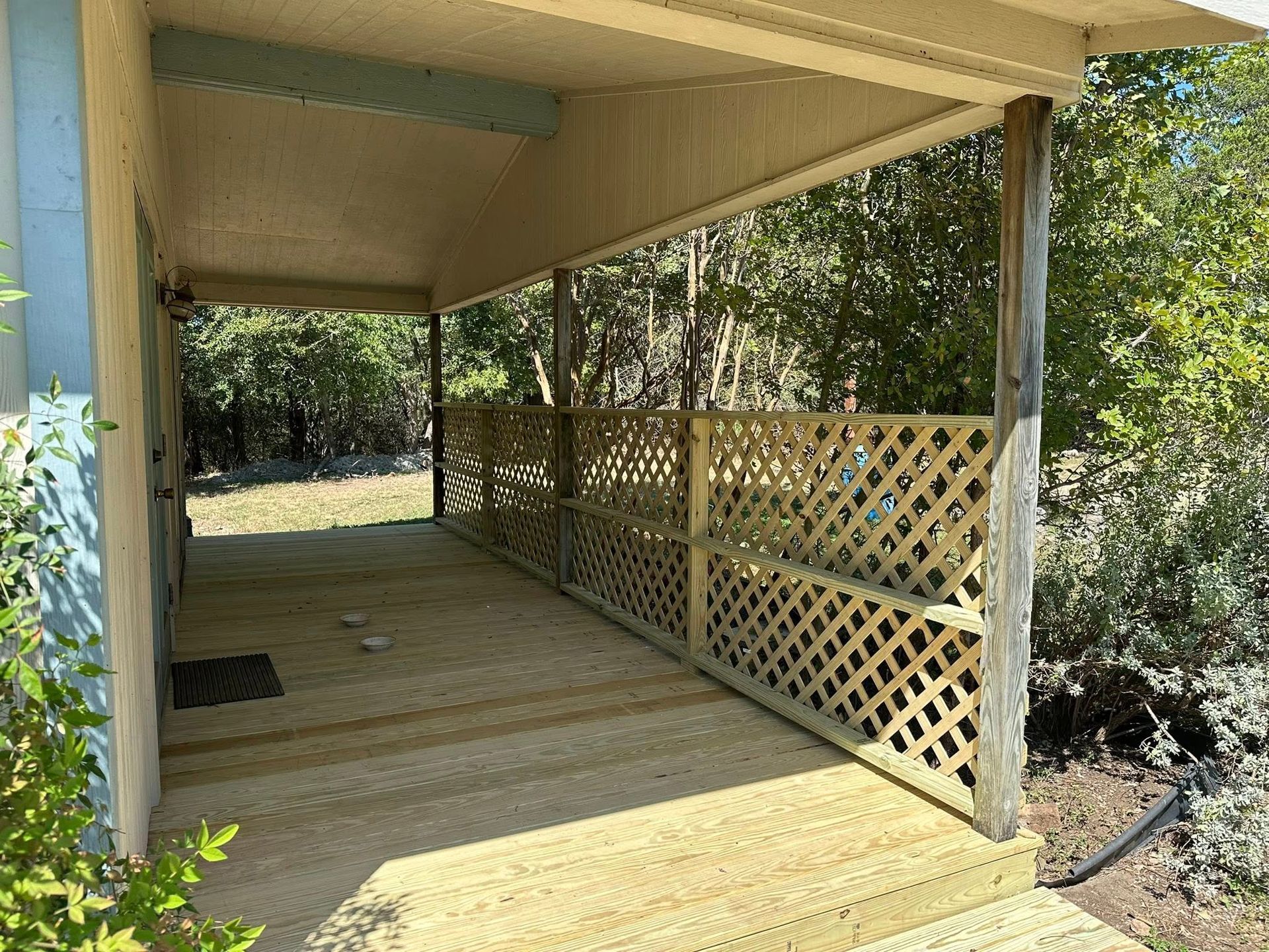Covered wooden porch with lattice railing beside trees and a yard