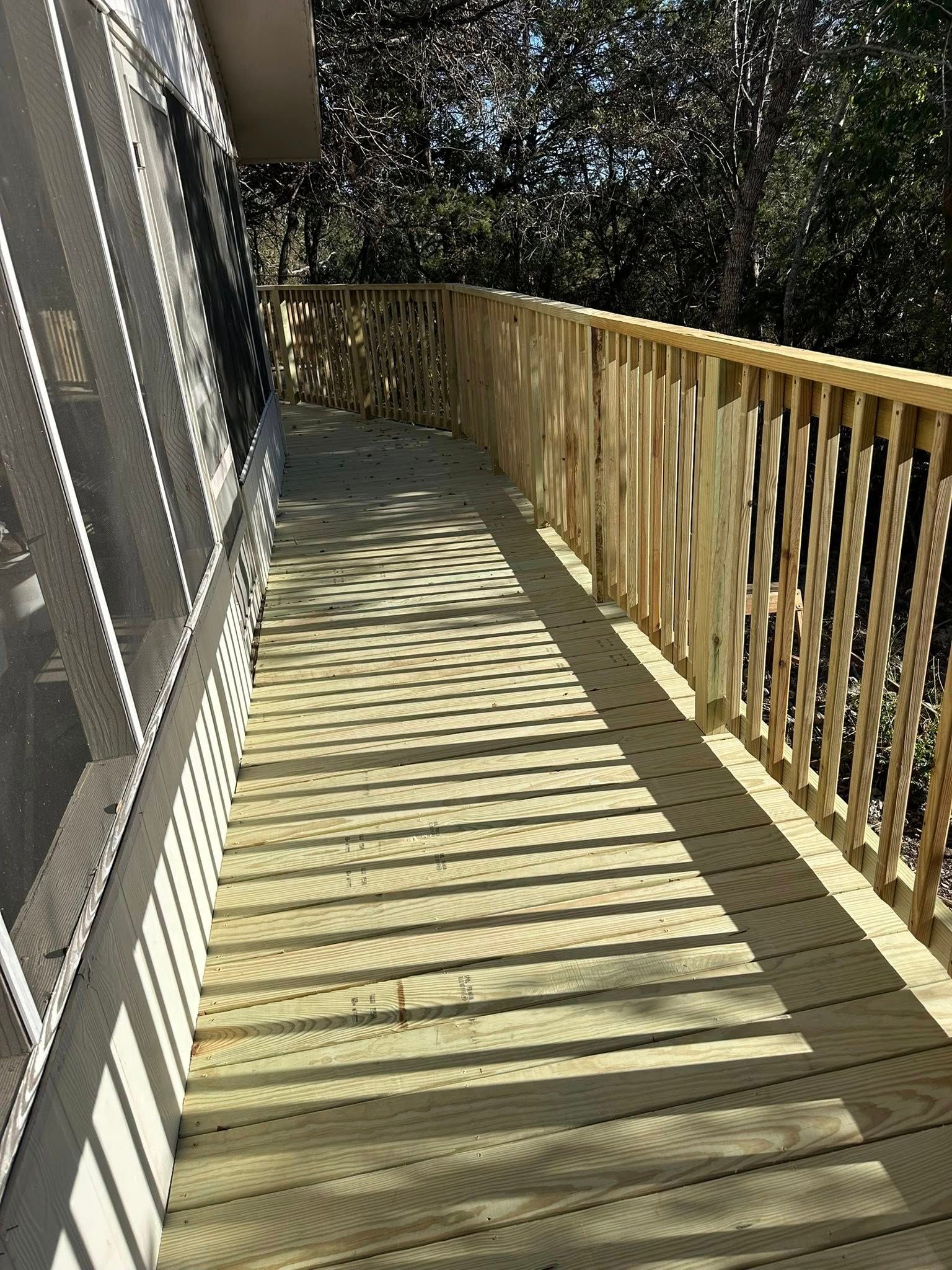 Wooden deck walkway beside a house, with railing and long striped shadows from the sun.