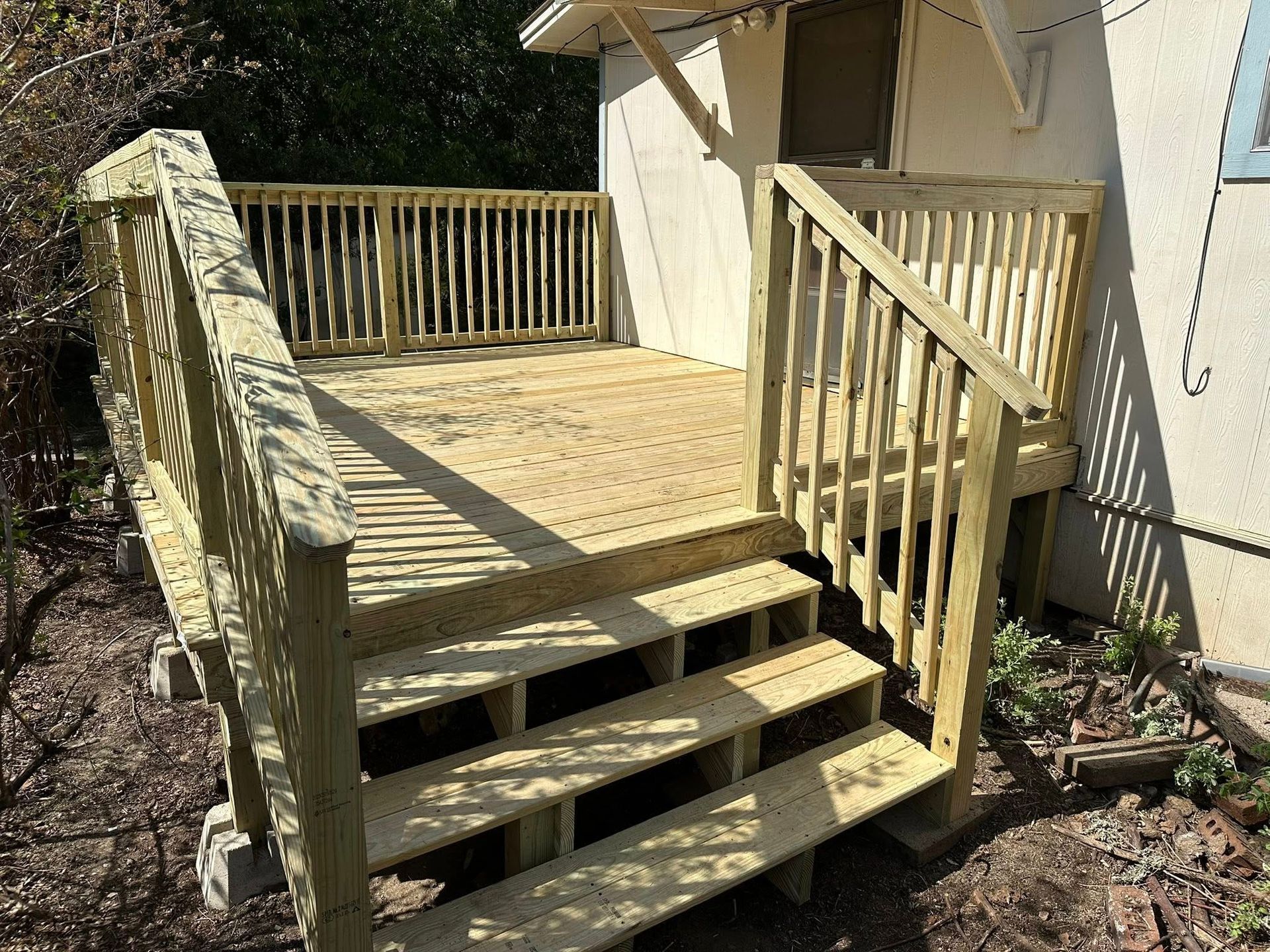 Wooden backyard deck with stairs, railing, and a small landing beside a house