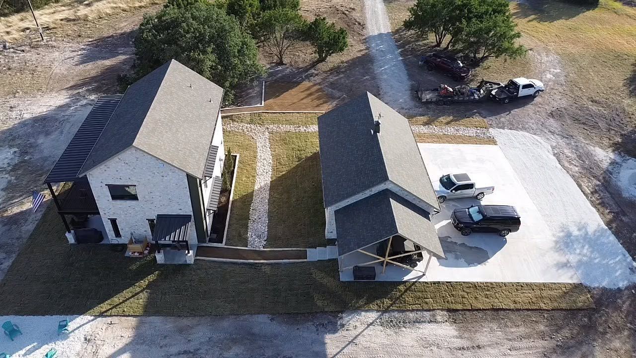 Aerial view of two small houses with driveways, parked cars, and a wooded yard.