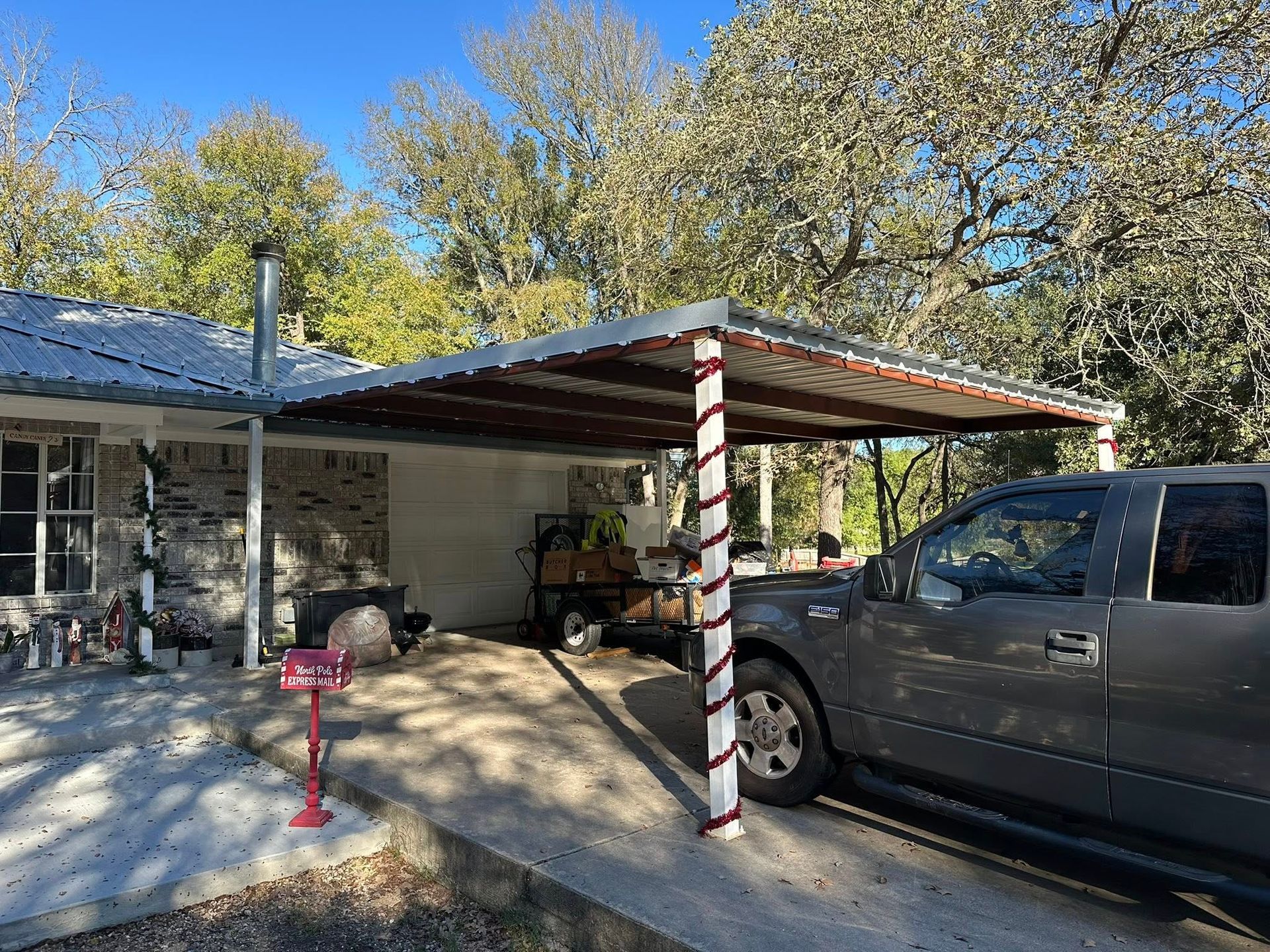 Truck parked under a red-and-white striped carport beside a house with trees in the background