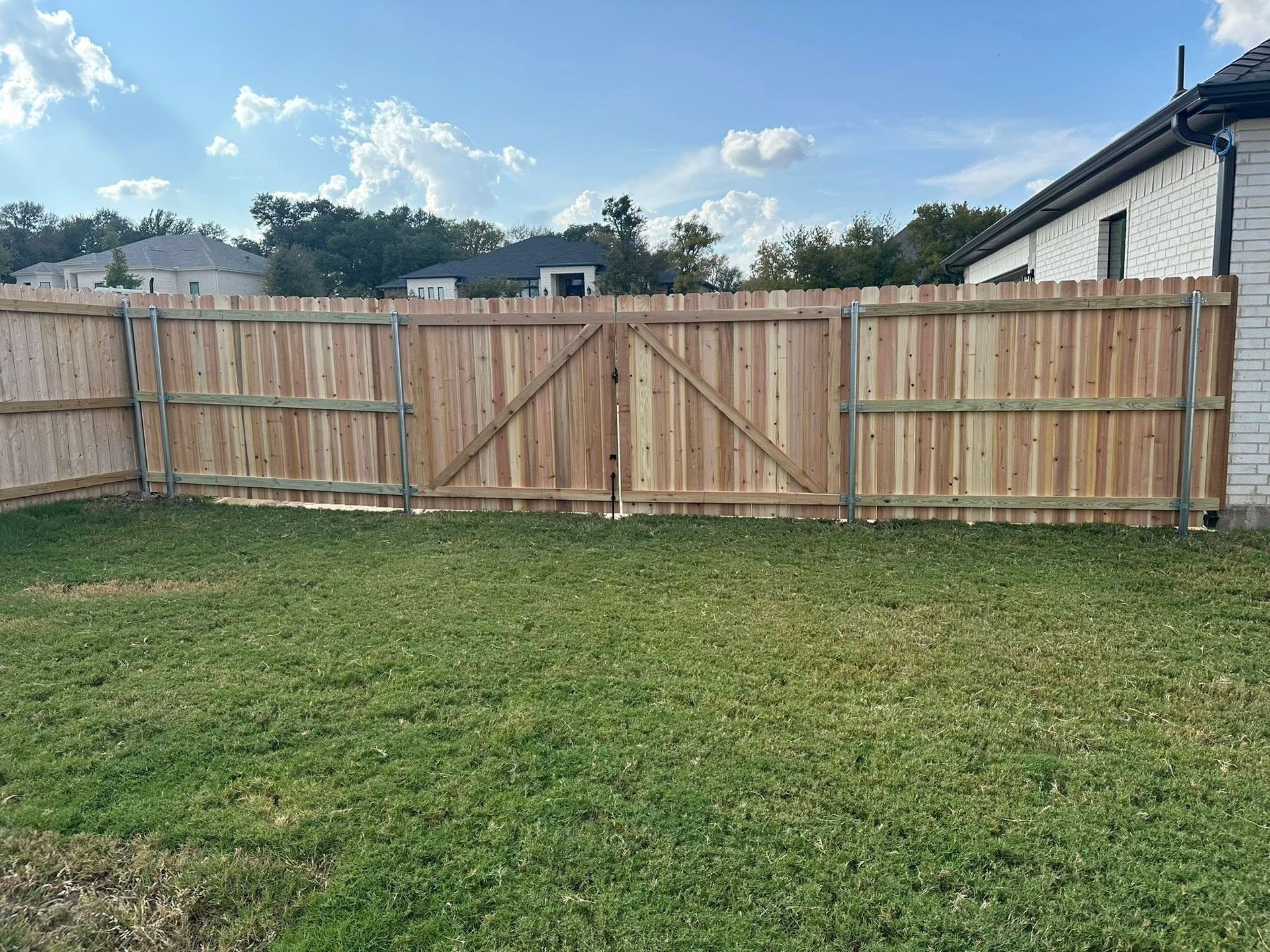 Wooden privacy fence with a double gate around a grassy backyard under a partly cloudy sky