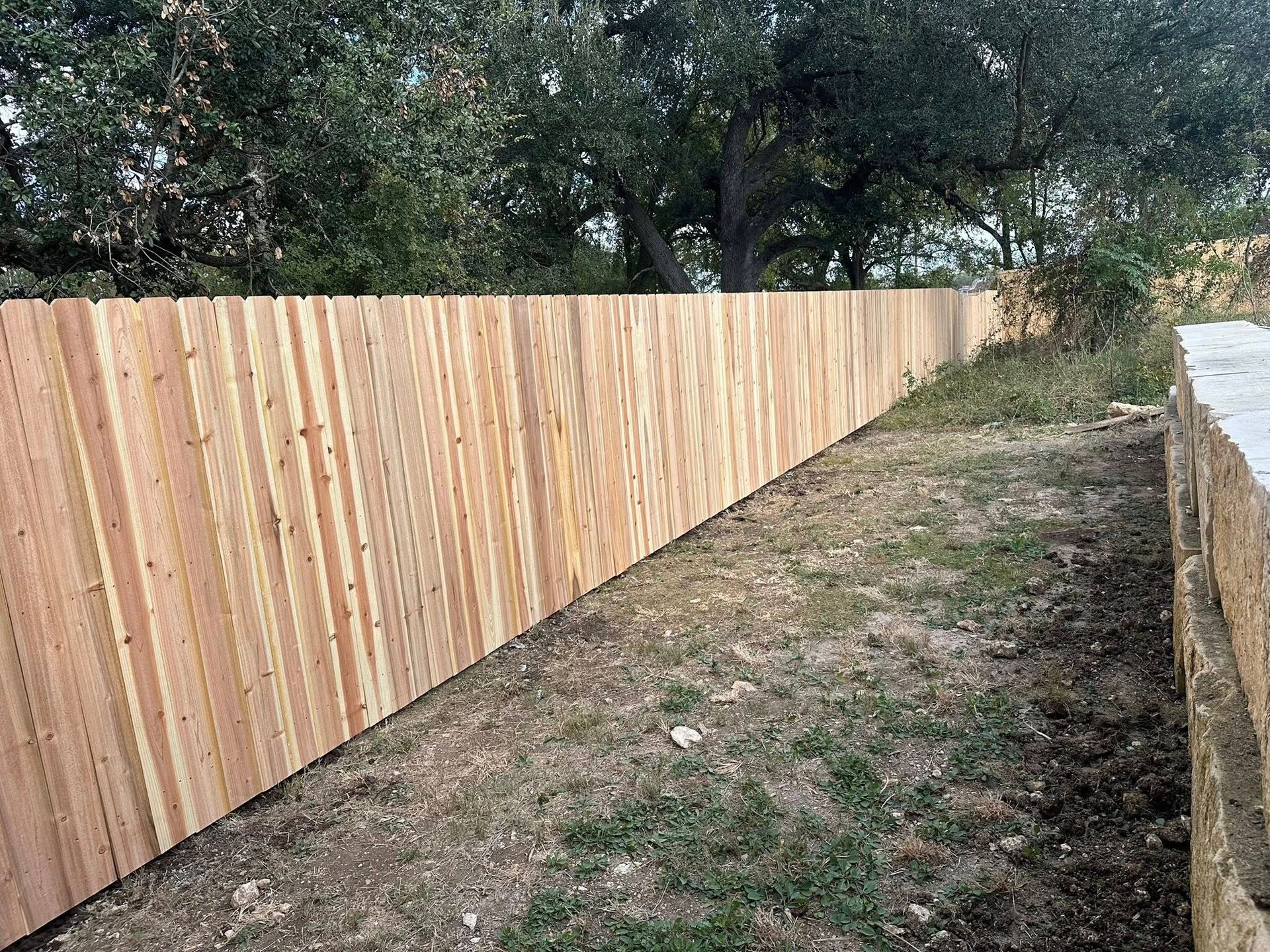 New wooden fence along a narrow dirt path beside trees and brush
