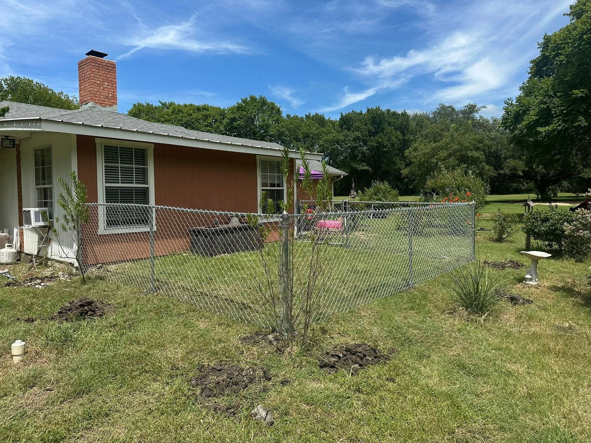 Small brick house with a fenced front yard and grassy lawn under a blue sky