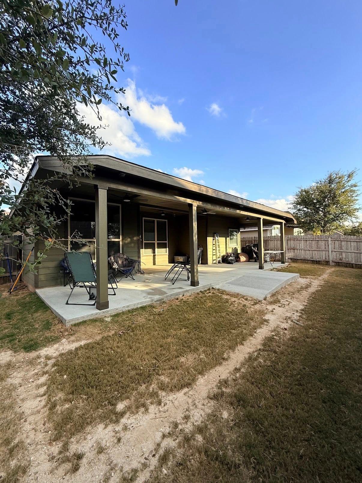 Open patio on a house with a covered porch, concrete slab, and grassy yard under a blue sky.