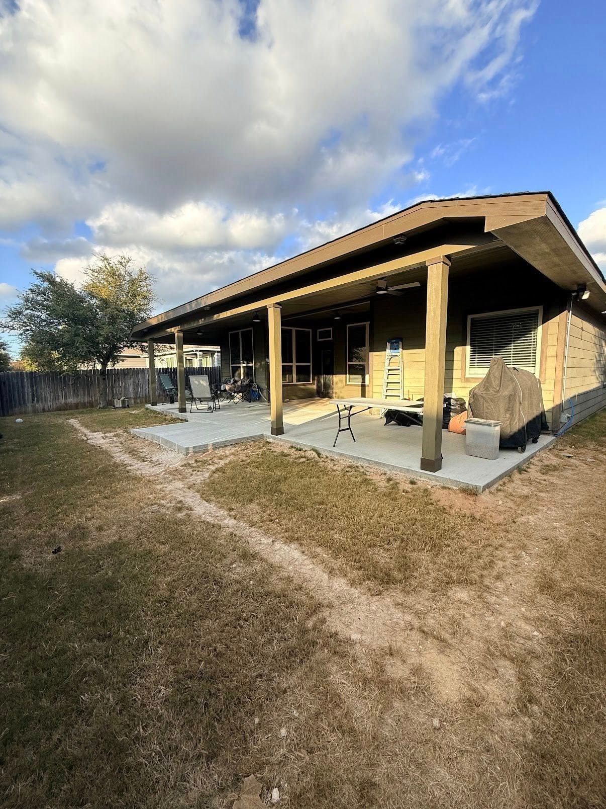 Single-story house with covered porch, patio chairs, and a grassy yard under a cloudy sky