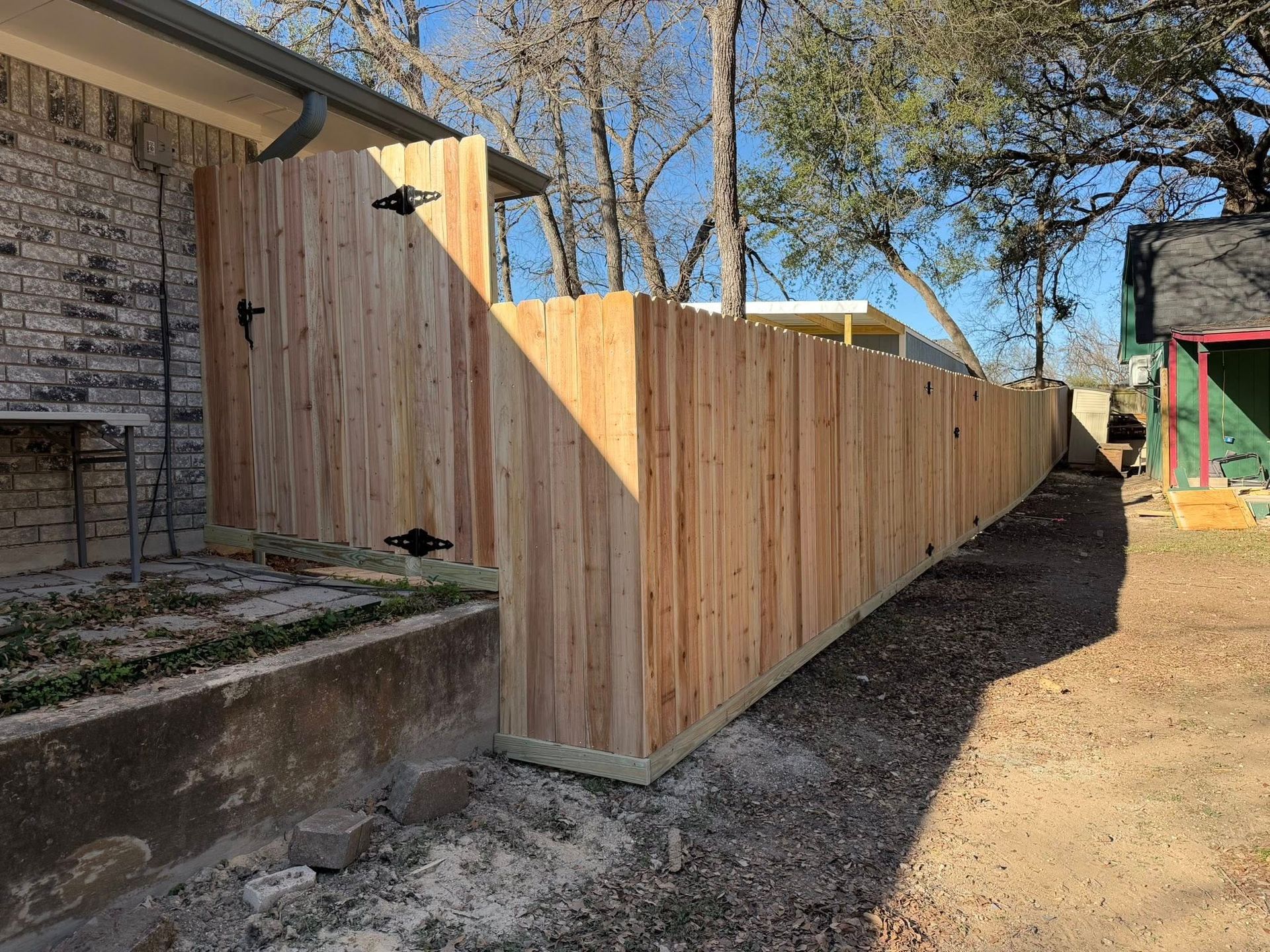 New wooden privacy fence along a concrete patio beside a brick house, in a backyard.