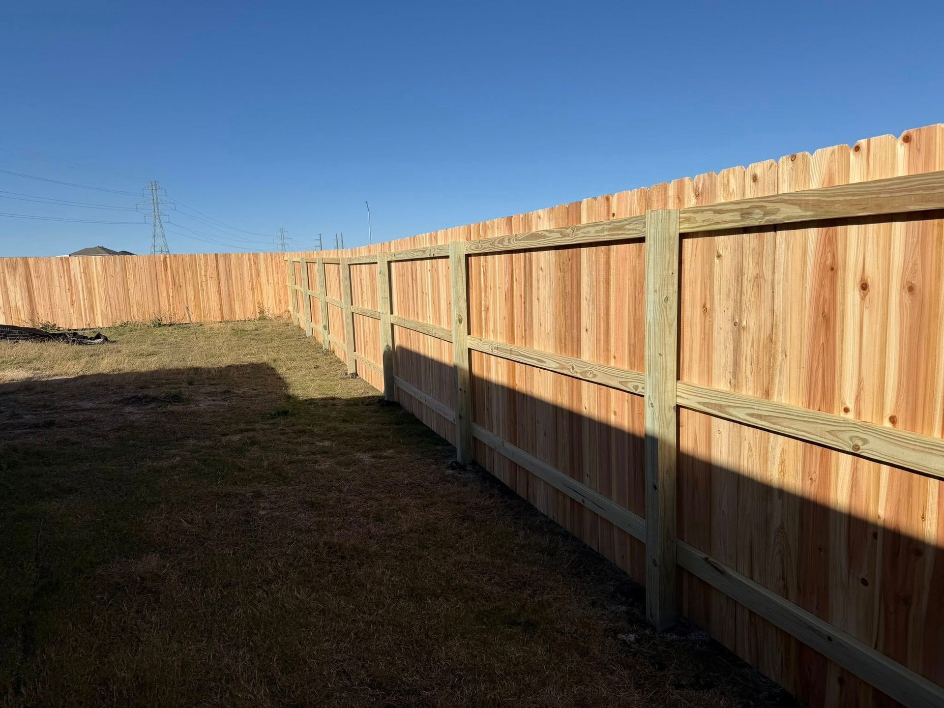 Long wooden fence along a grassy yard under a clear blue sky.