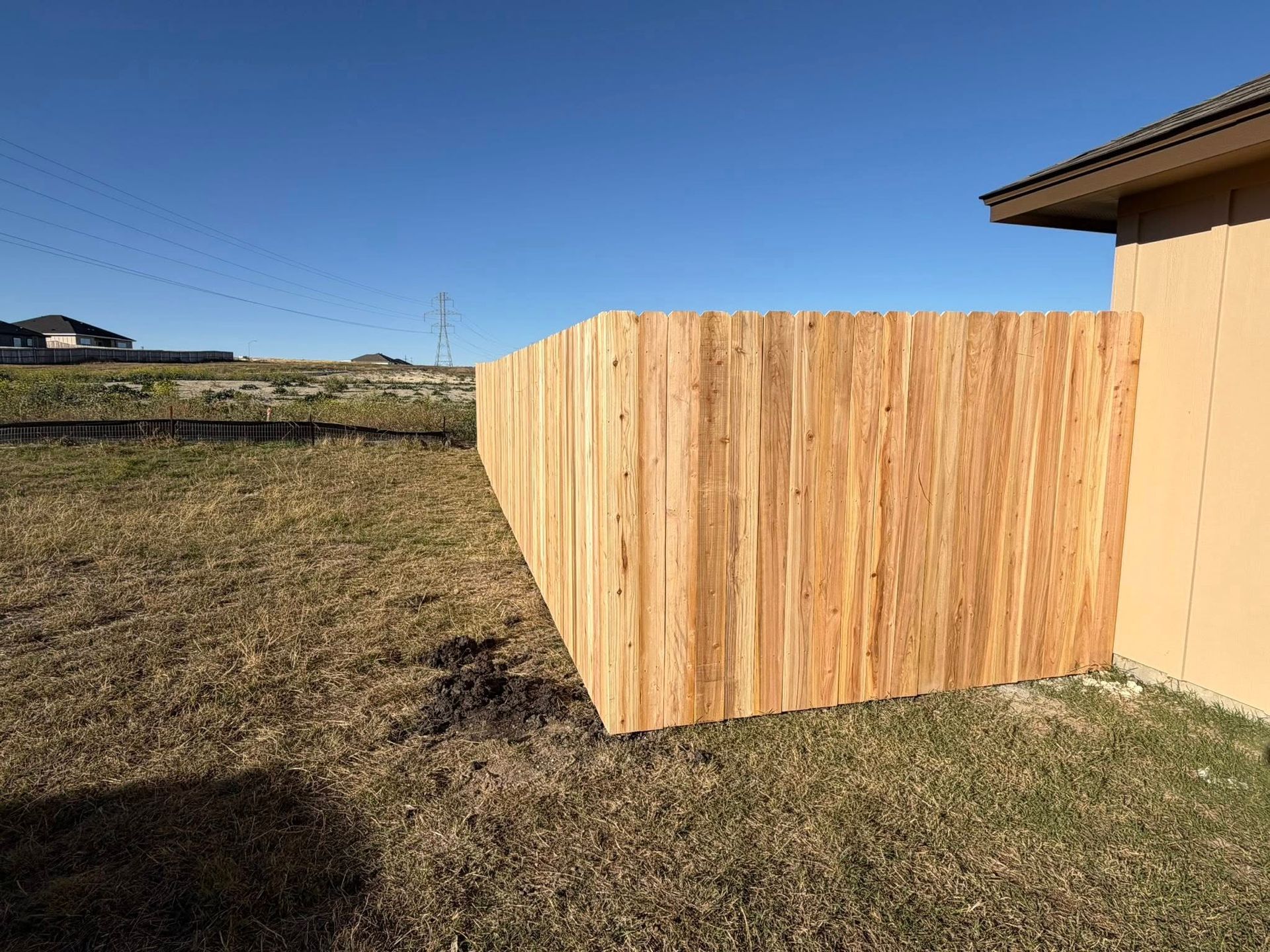 Wooden fence panels beside a beige house in a grassy yard under a clear blue sky