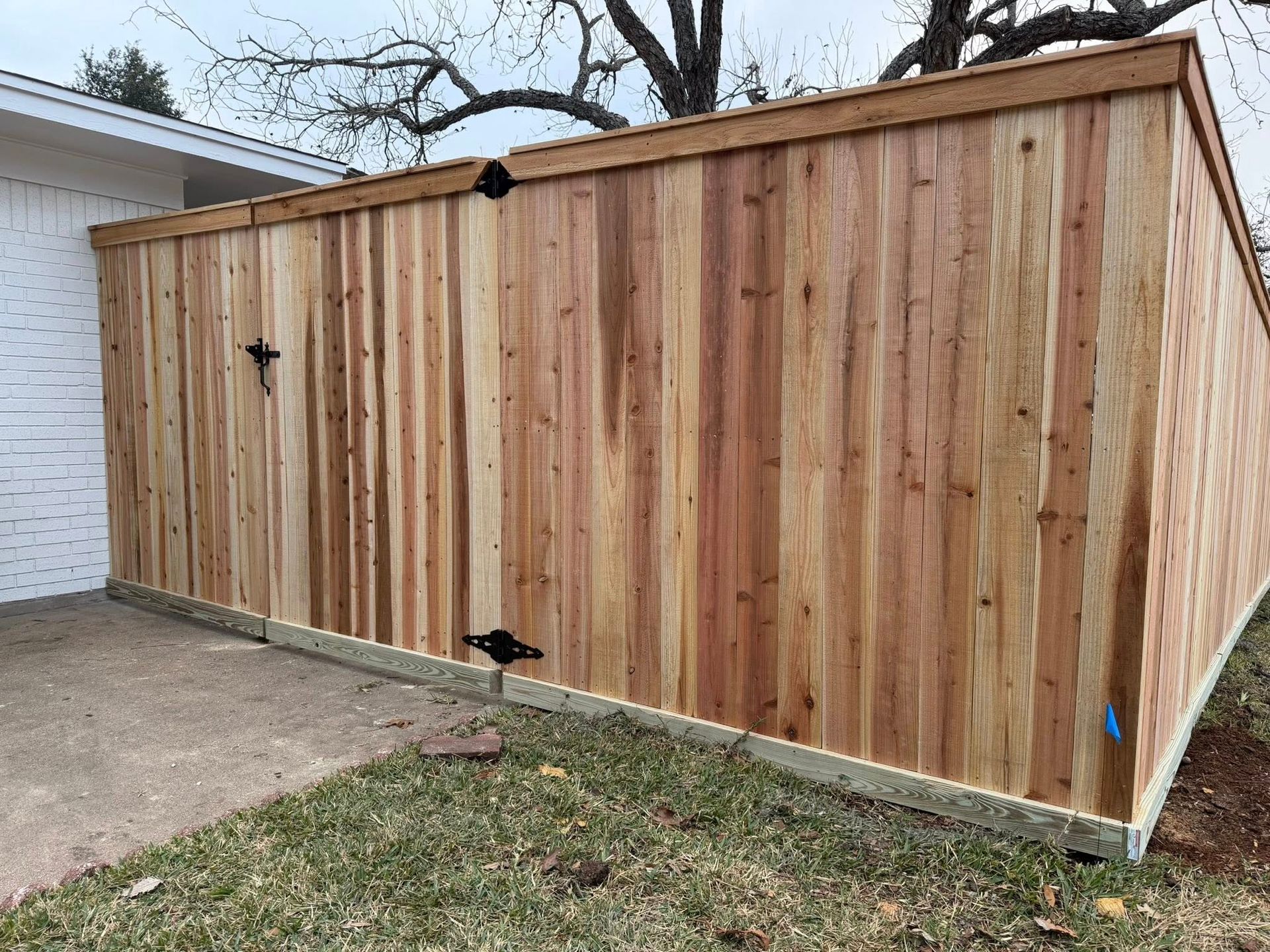 Wooden privacy fence panel leaning along a driveway beside a house, with grass in front.