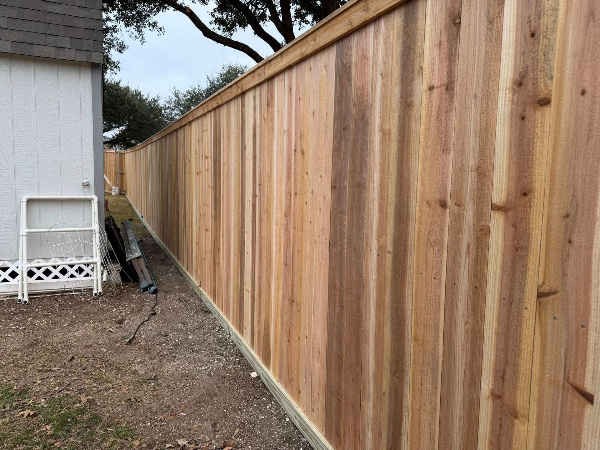 Freshly built wooden privacy fence along a house and narrow dirt yard