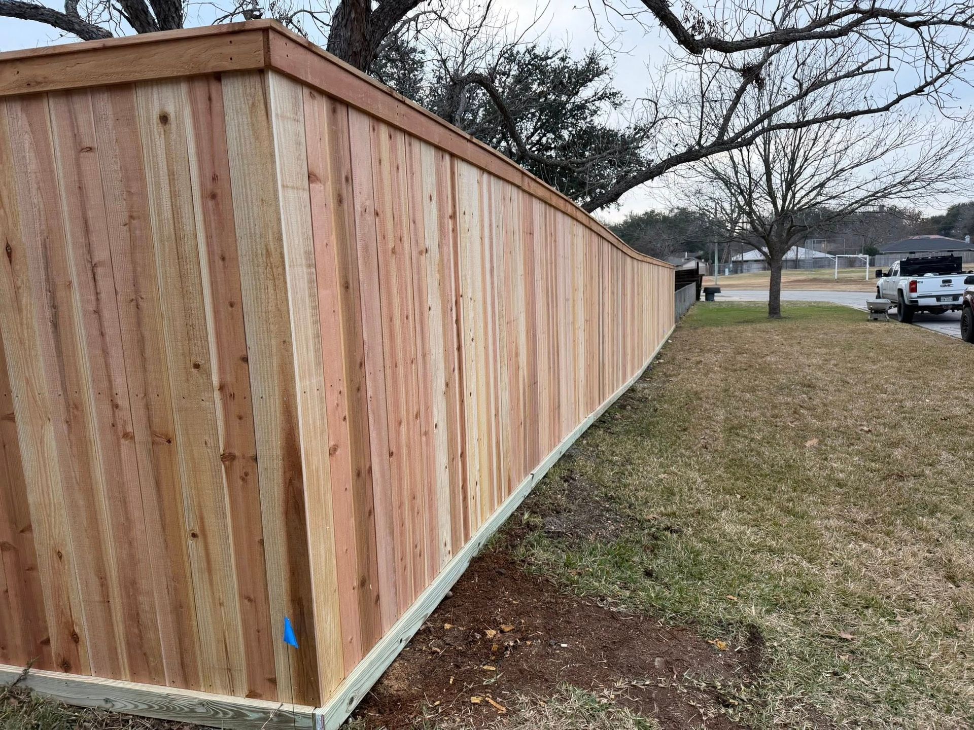 Long wooden privacy fence beside a grassy yard, extending into the distance under a cloudy sky.