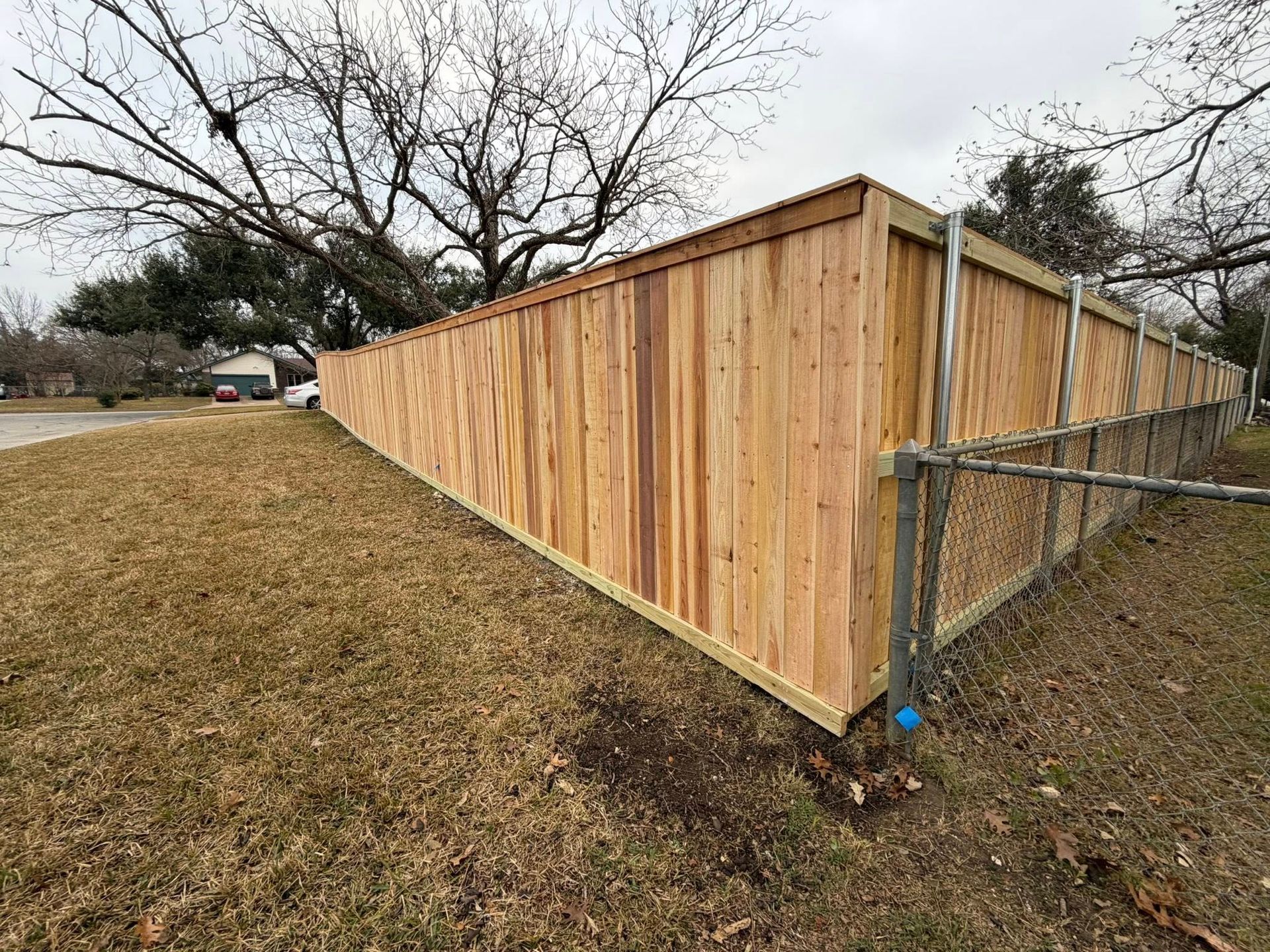 Wooden privacy fence along a grassy yard with leafless trees in the background