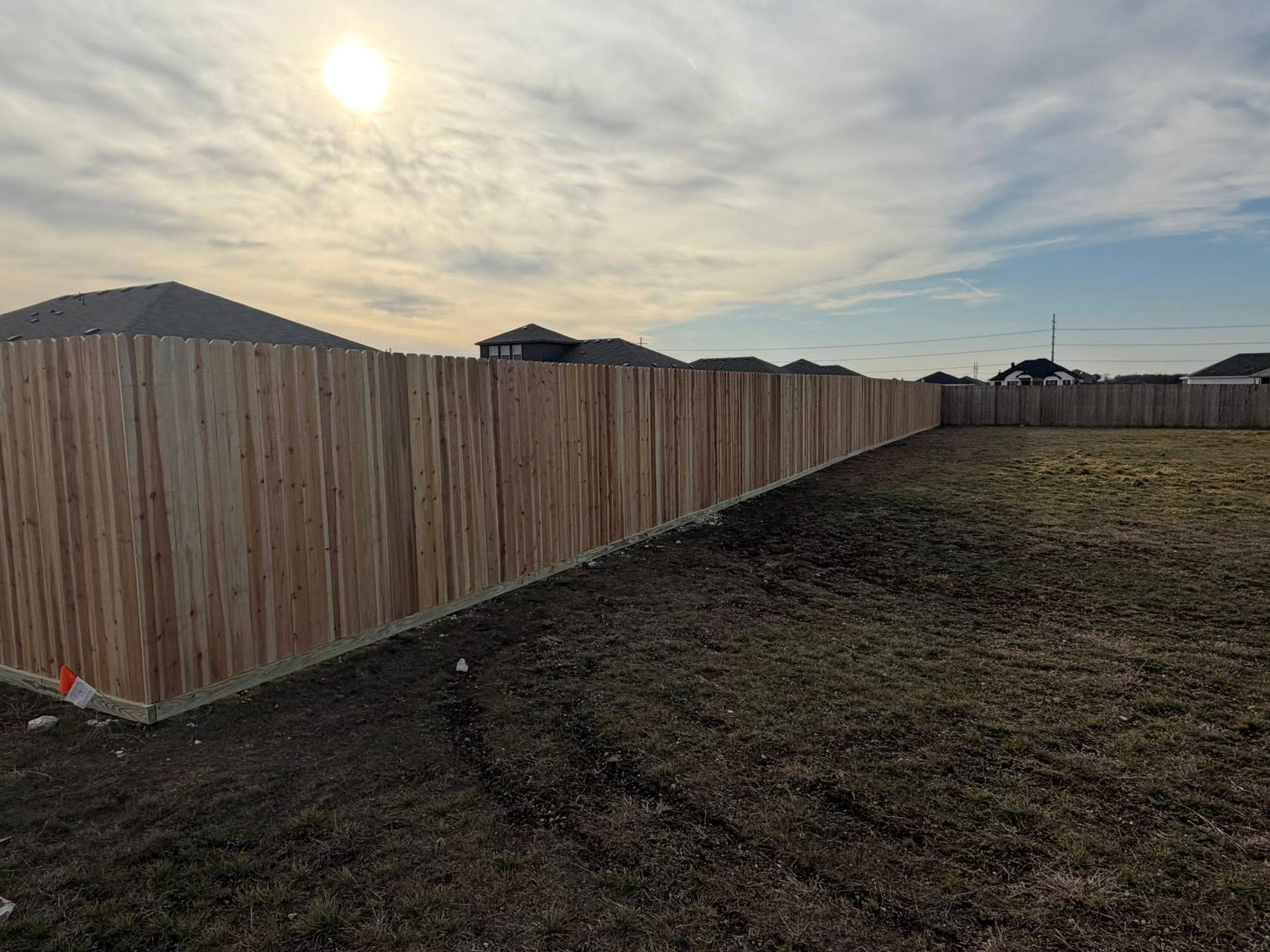 Wooden privacy fence along a dirt lot at sunset, with mountains and cloudy sky in the background