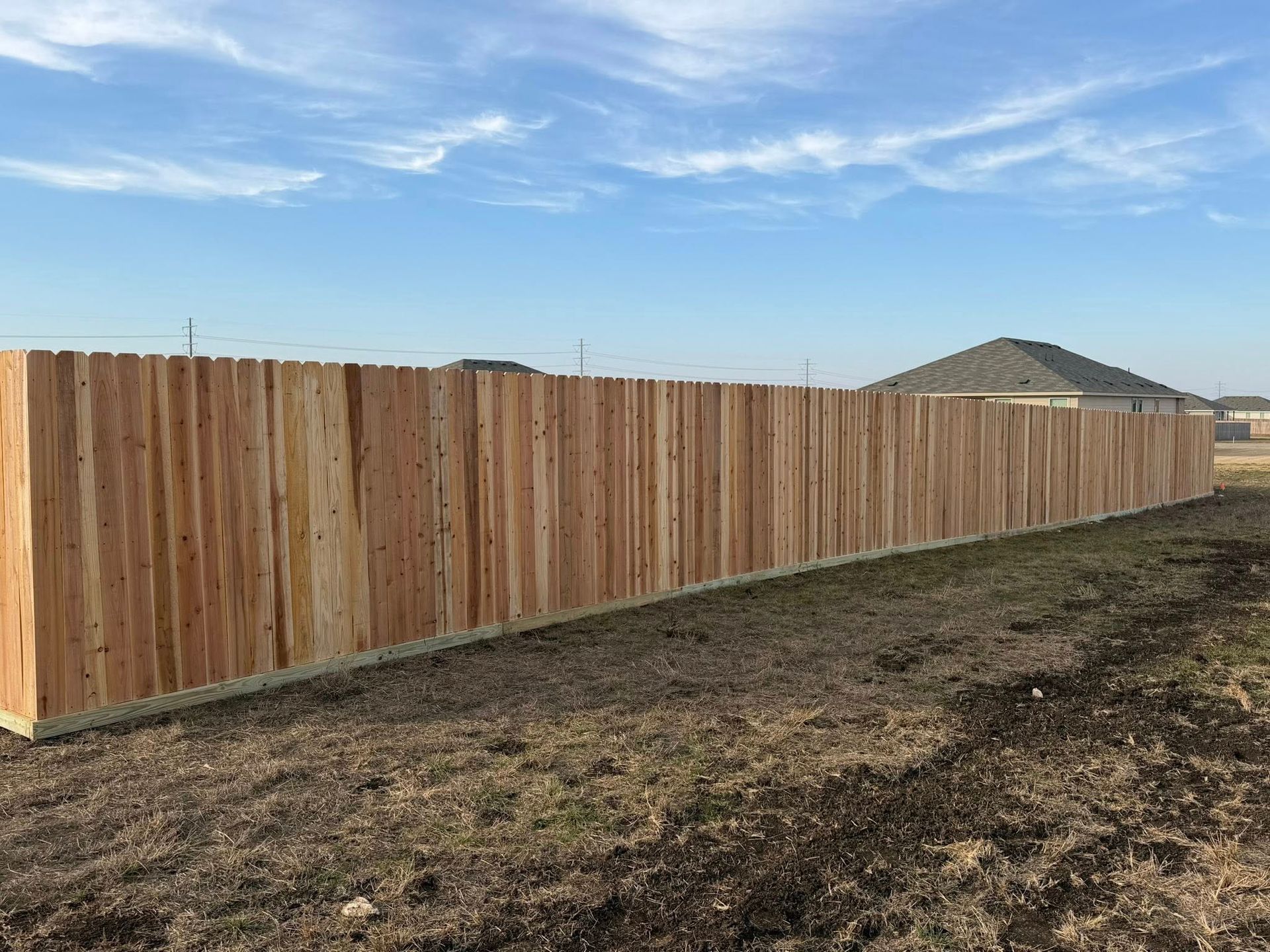 New wooden fence lining a dirt lot under a blue sky