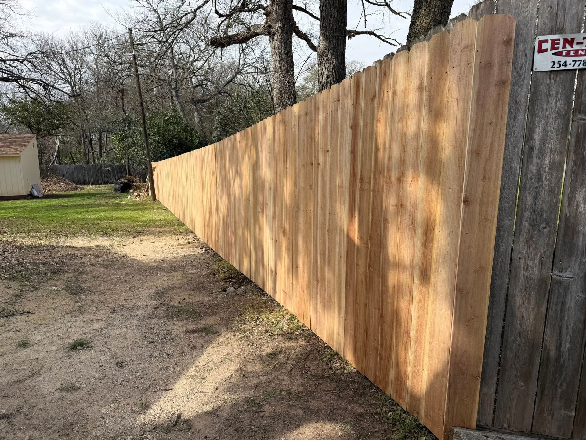Long wooden privacy fence along a dirt path in a wooded yard