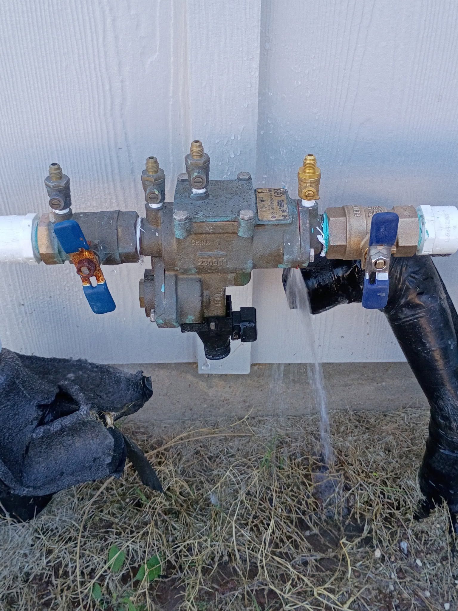 Outdoor water valve manifold with multiple shutoff valves and hoses attached to a house wall.