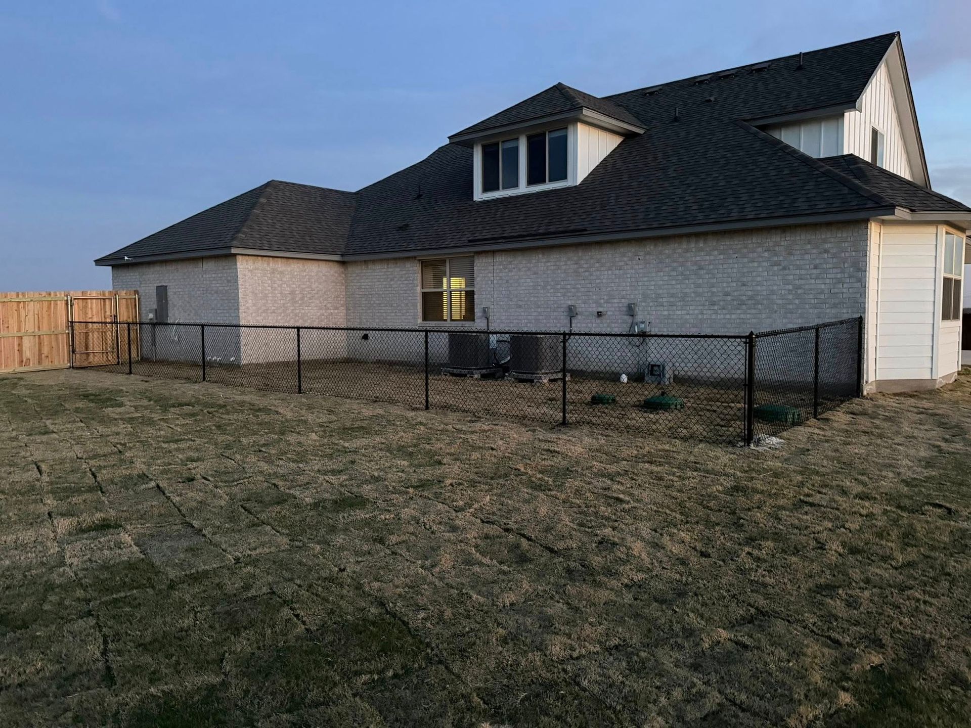Suburban house with black roof and white siding, fenced backyard at dusk