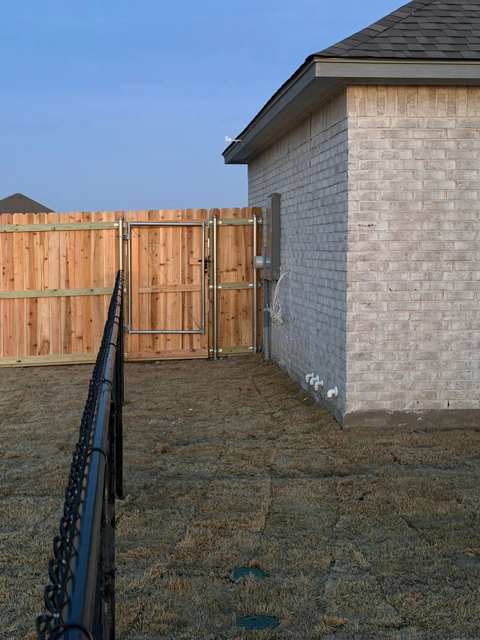 Backyard with a wooden fence gate beside a brick house and a chain-link fence in the foreground