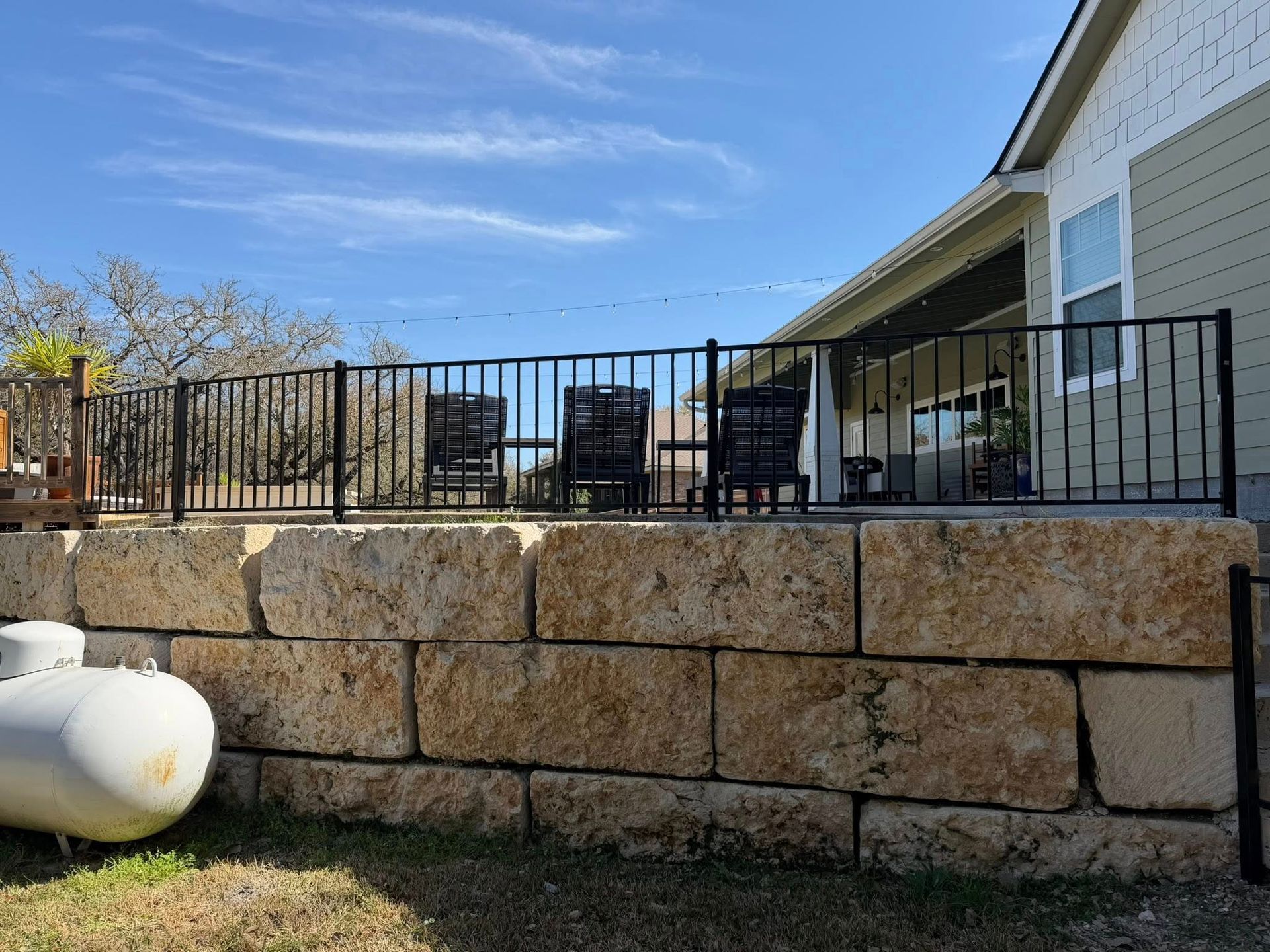 Patio with black metal railing atop a stone retaining wall under a blue sky
