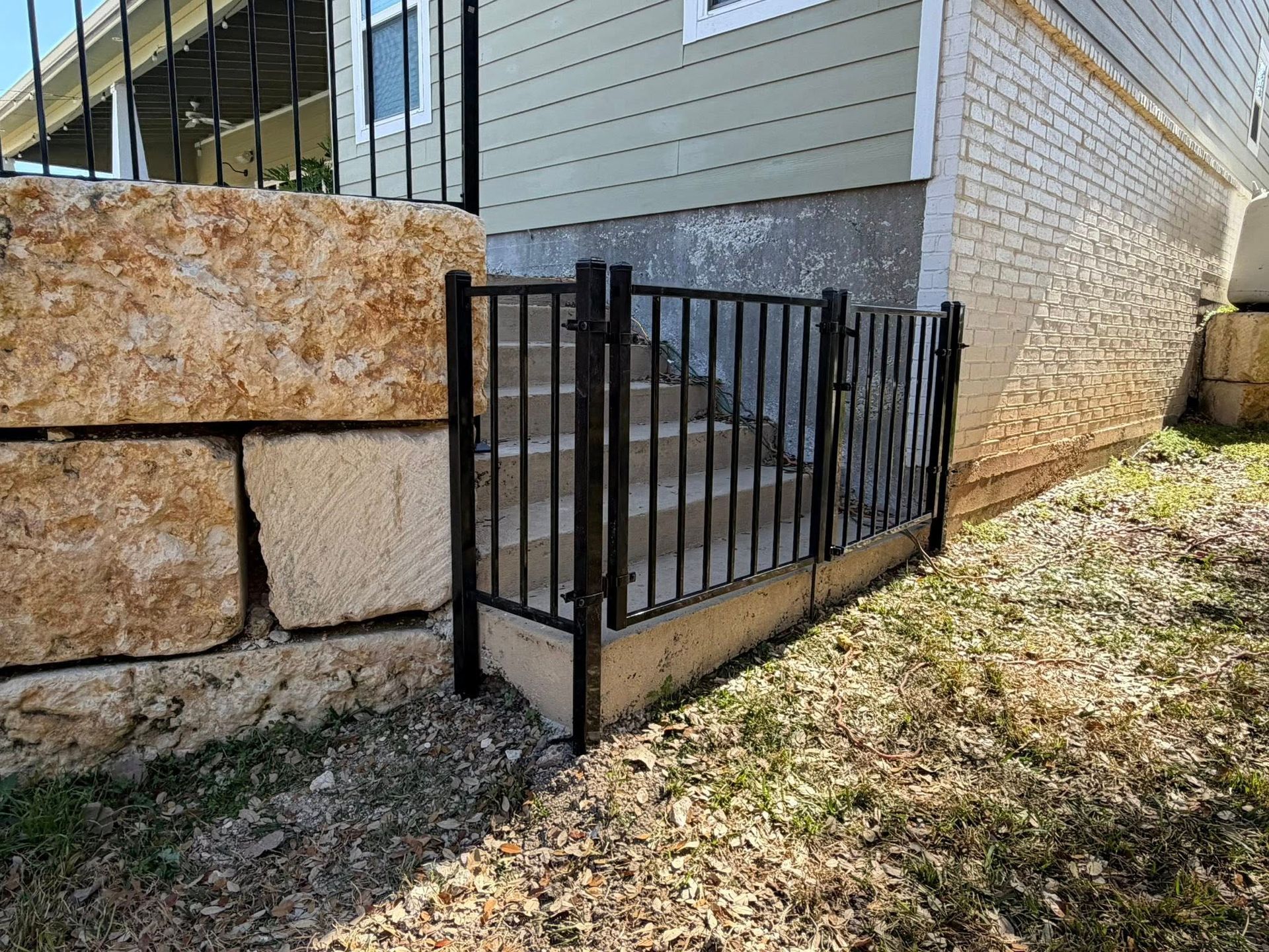 Black metal railing enclosing a concrete basement stairwell beside a stone and siding house.