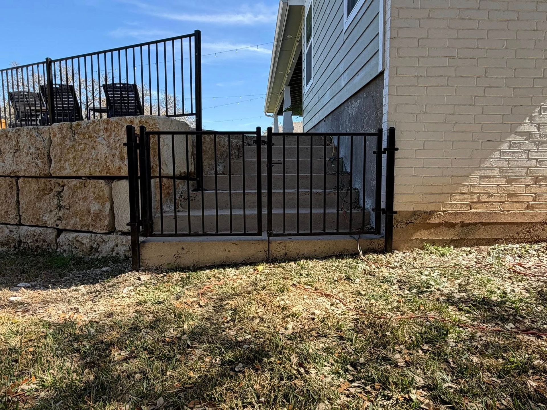 Black metal gate beside a stone wall and house exterior in a backyard yard area