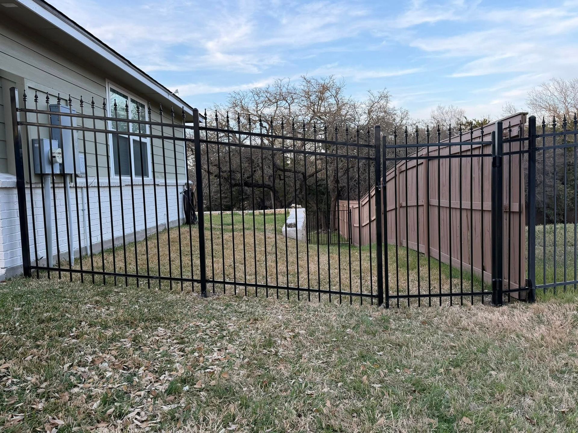Black metal fence beside a house and brown retaining wall in a leaf-covered yard