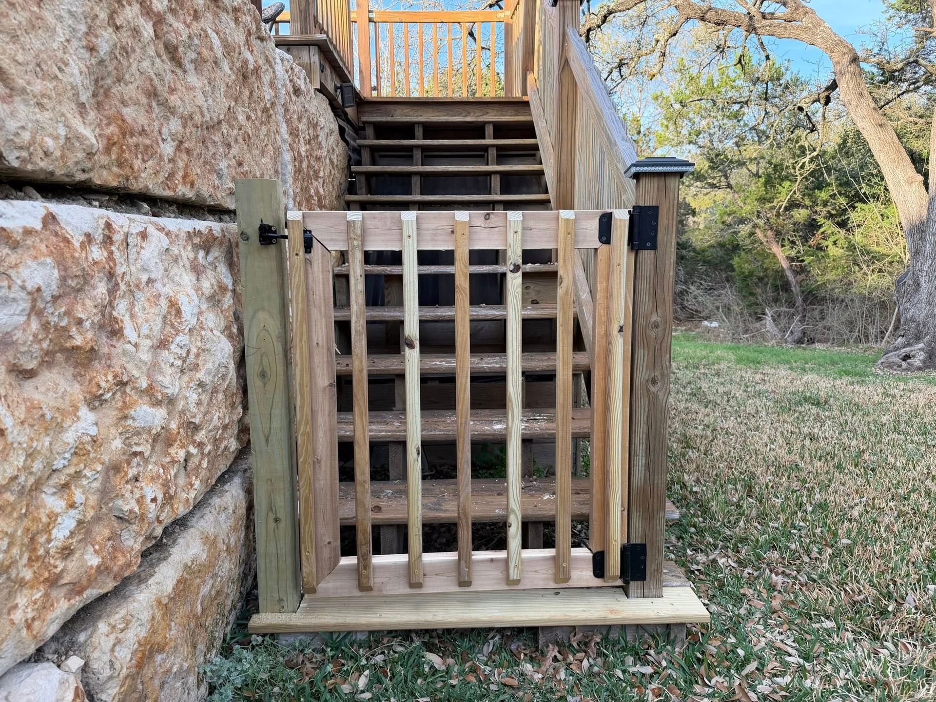 Wooden gate at bottom of outdoor stone stairway with black latch posts and grassy yard beyond