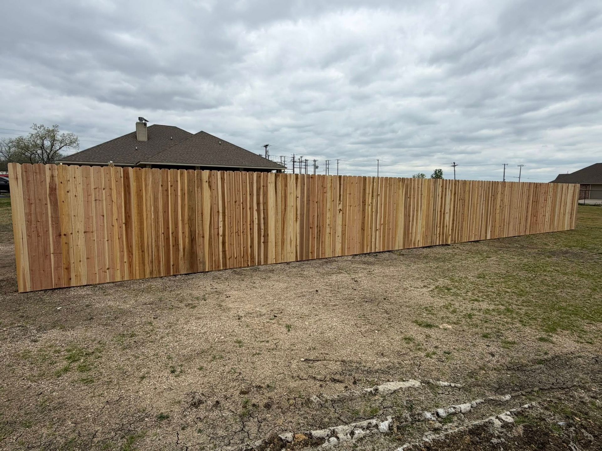 Wooden privacy fence along a dirt lot under a cloudy sky